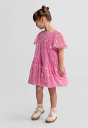 Side view of girl wearing pink tulle dress with floral embroidery, flutter sleeves and tiered skirt, styled with sneakers against white background