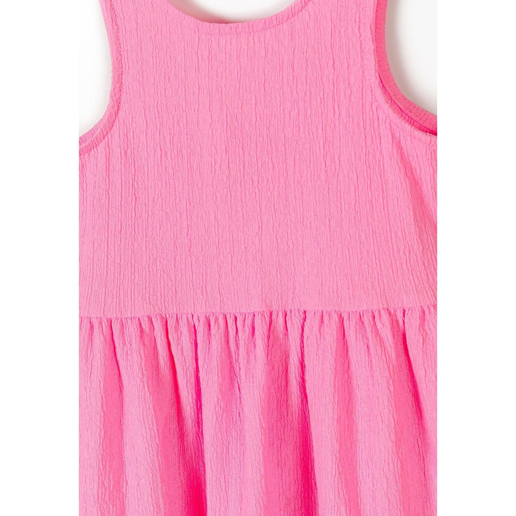 Close-up detail of pink dress showing textured fabric, sleeveless bodice and gathered tiered skirt construction