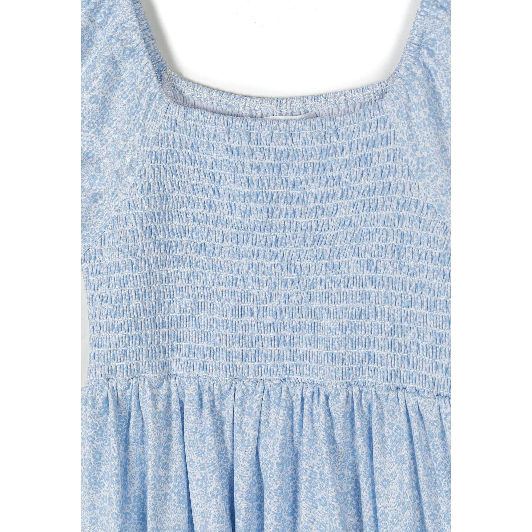 Close-up detail of smocked bodice showing elastic shirring texture and square neckline construction on light blue floral fabric