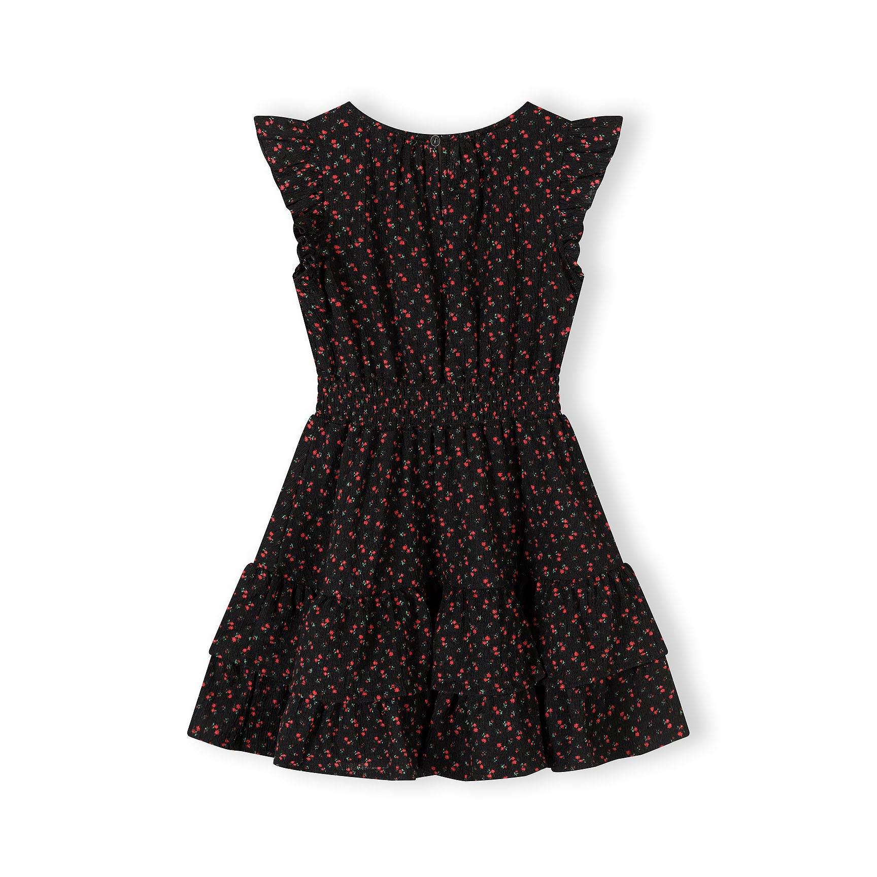 Flat lay view of black A-line dress with small red floral pattern and frill sleeves on white background showing full garment details