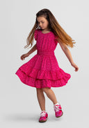 Young girl twirling in a pink floral dress with frill sleeves and tiered elasticated waist, showcasing playful design.