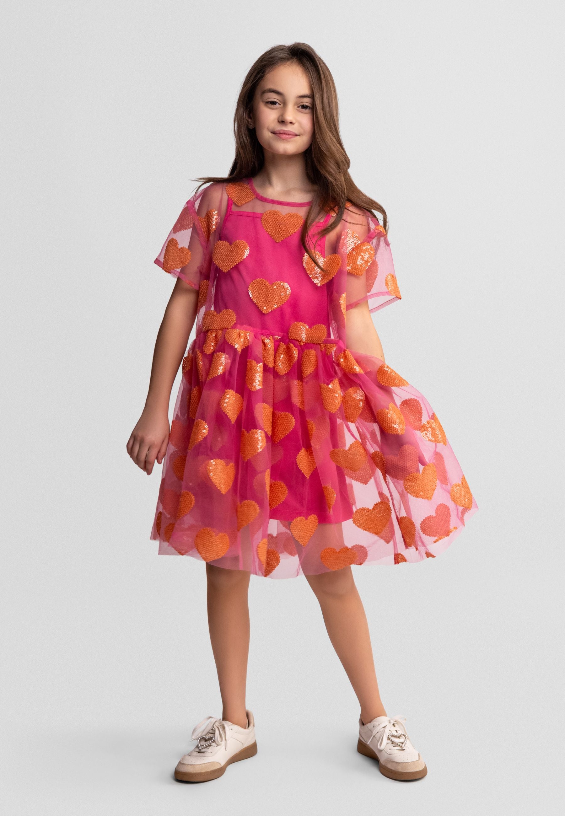 Flat lay of pink tulle dress with orange sequin hearts, showing short sleeves and gathered skirt design on white background