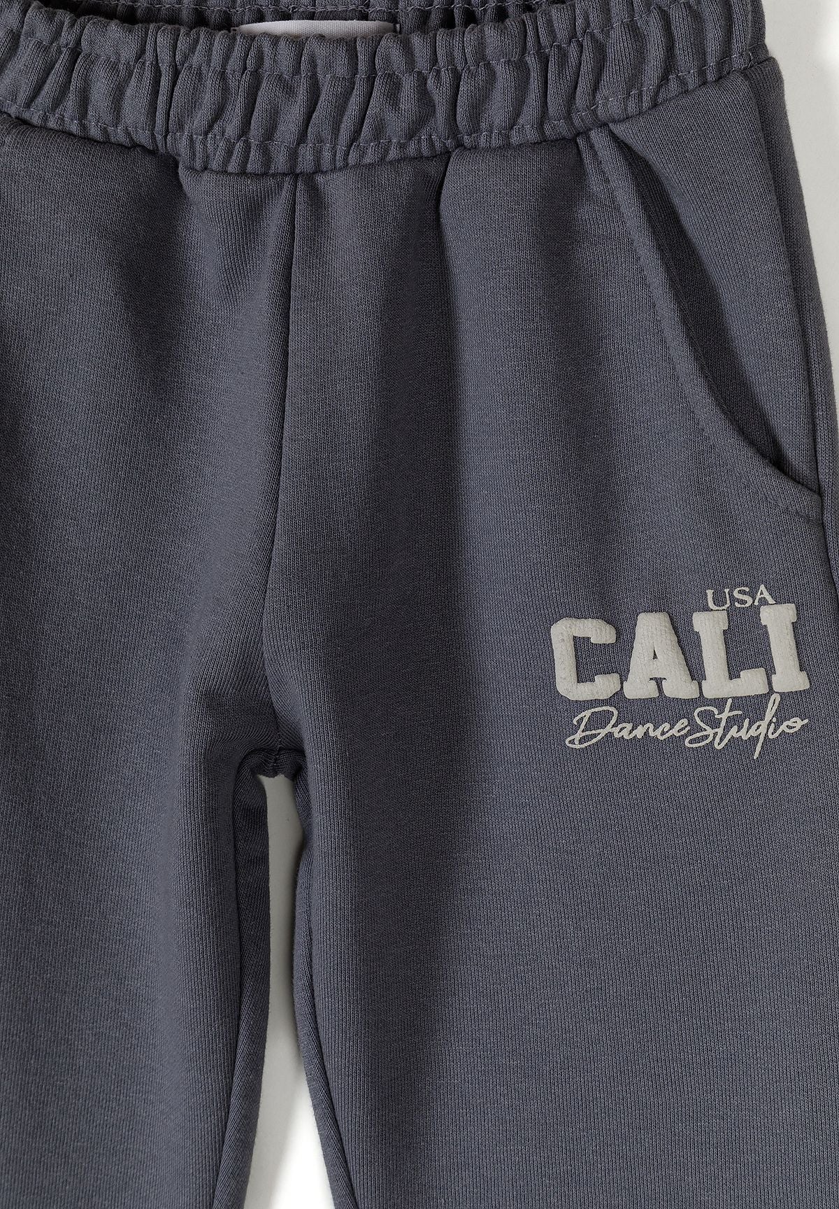 Detail of grey tapered jogging trousers with elasticated waistband and logo.