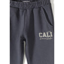 Close-up of blue-grey tracksuit bottoms showing elastic waistband and CALI USA Dance Studio text print on the leg