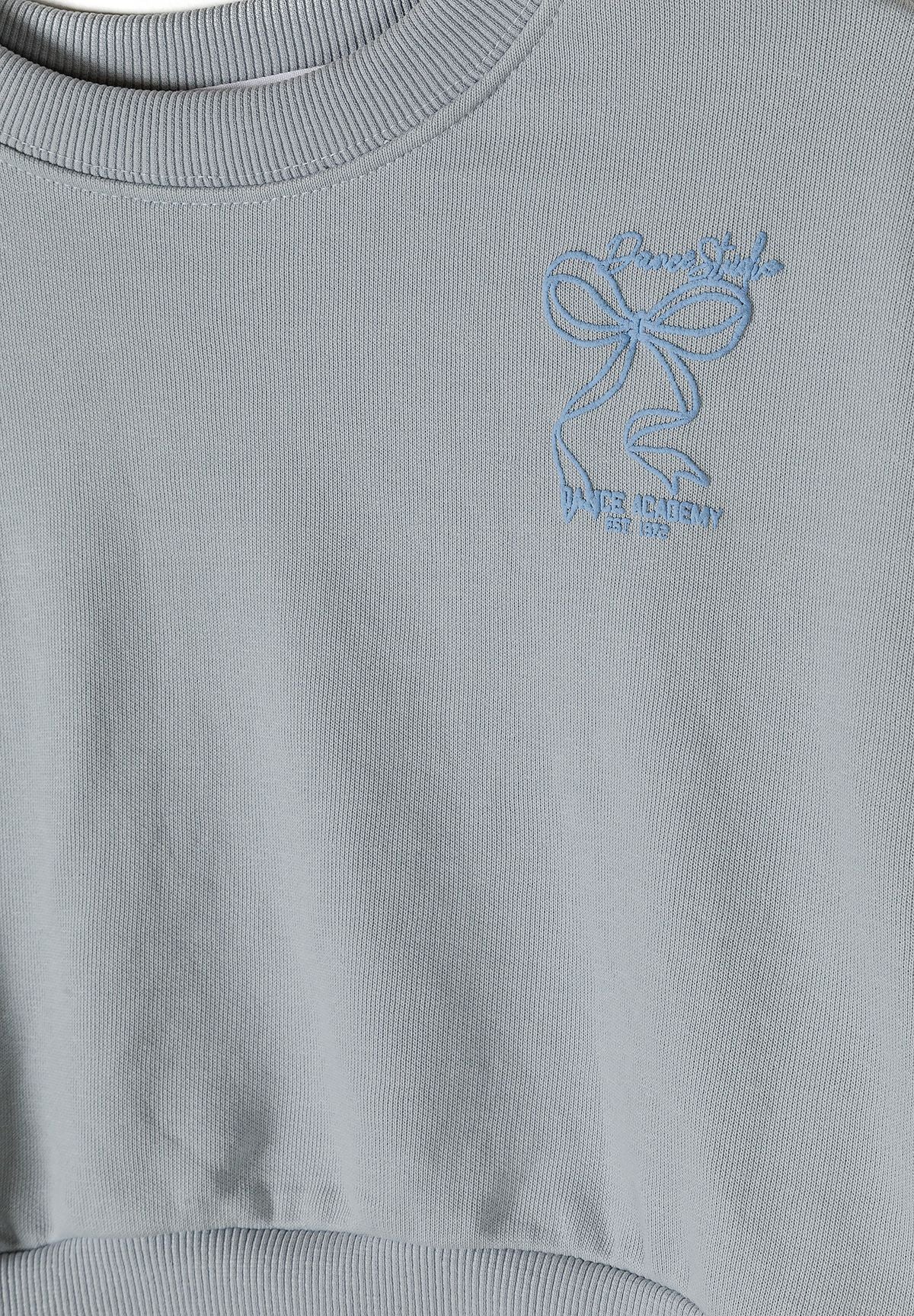 Detail of a light blue girls' tracksuit with a logo embroidery.