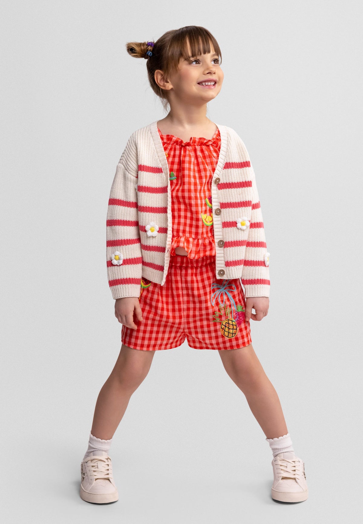 Girl wearing ivory and coral striped cardigan with white daisy motifs.