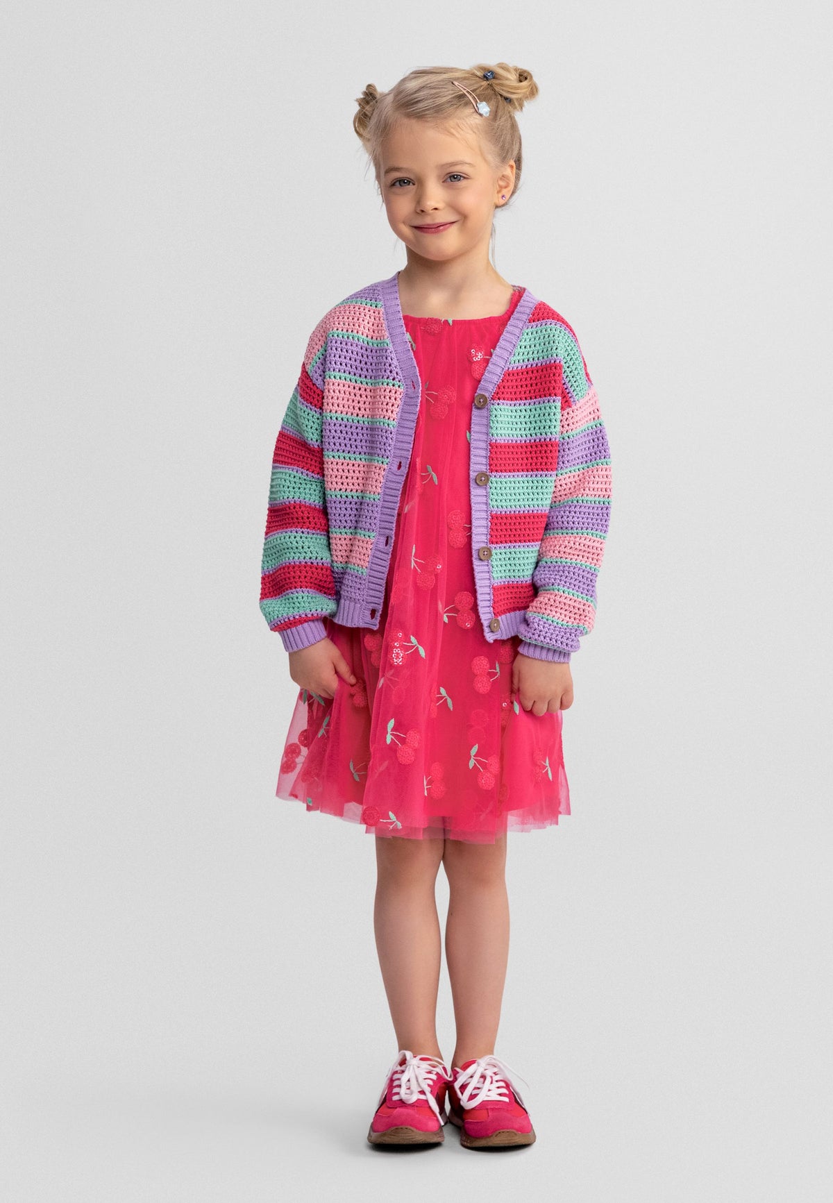Girl wearing pastel striped open-knit cardigan over a bright pink dress.