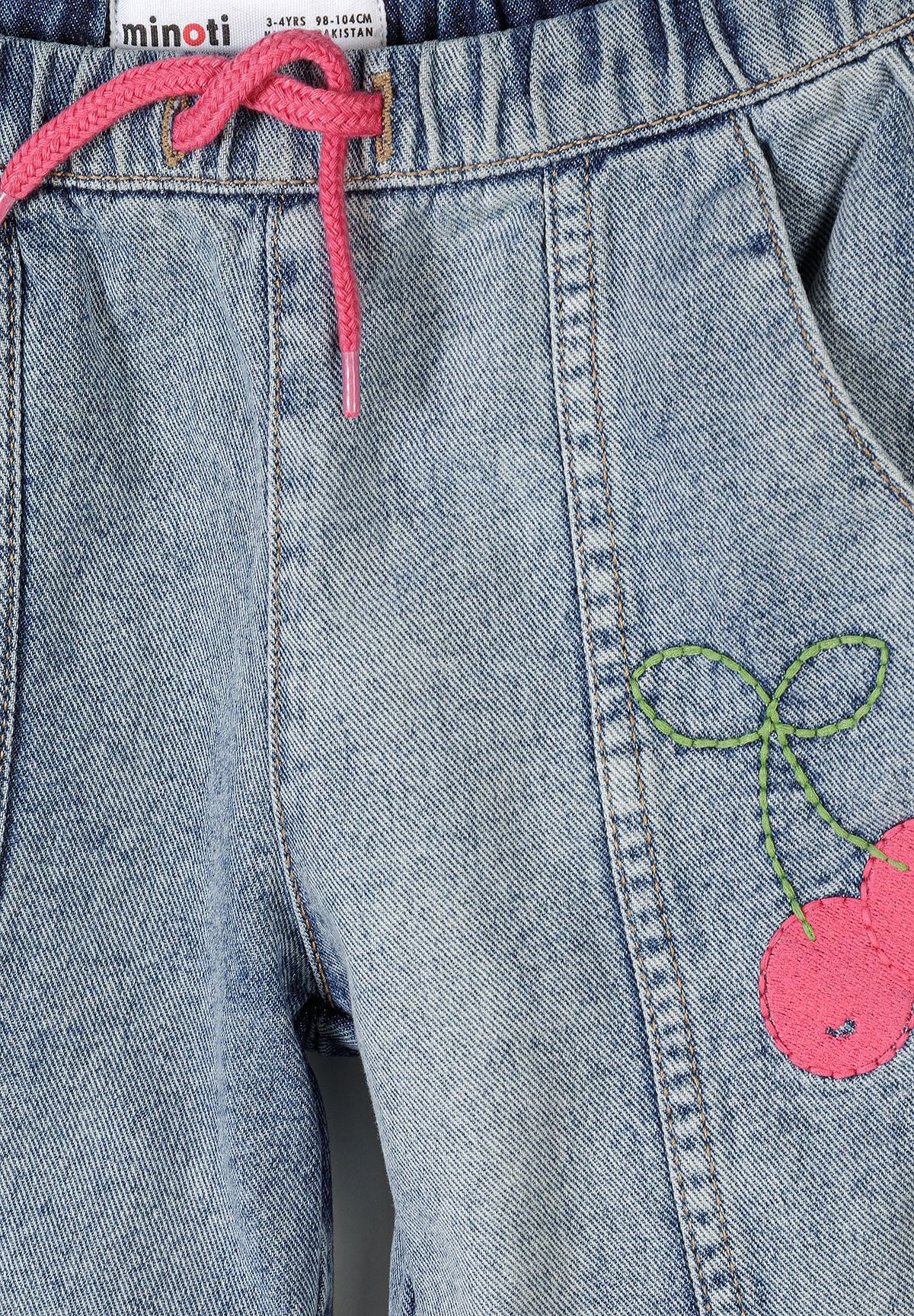 Detail shot of blue denim jeans waistband area showing Minoti label, pink drawstring and embroidered cherry design with green leaves