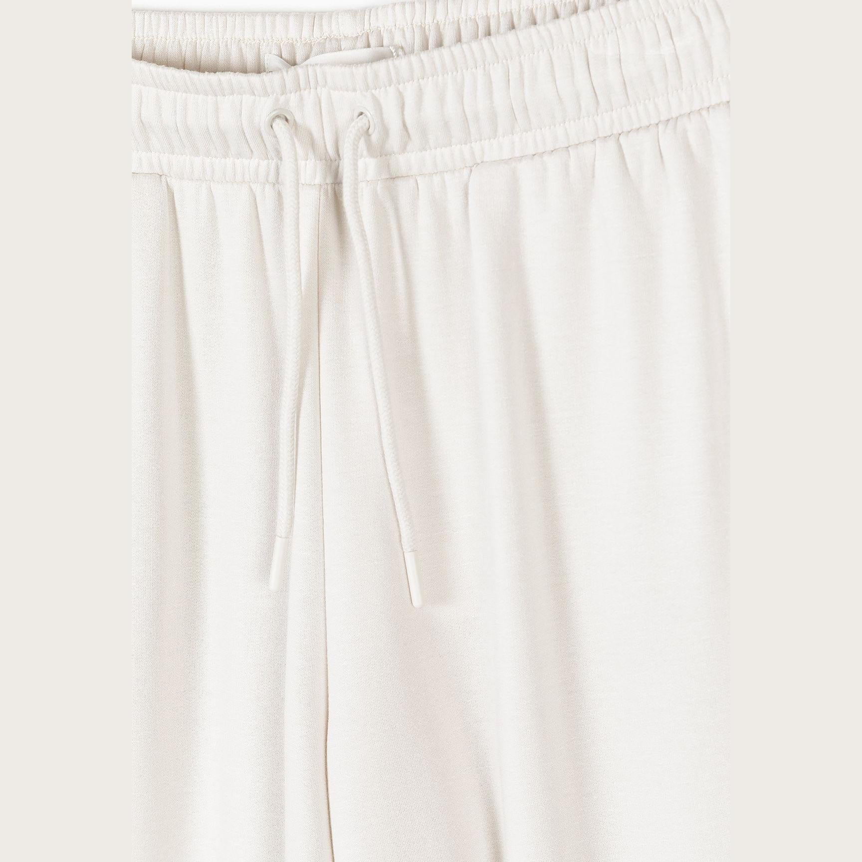 Close-up detail of waistband showing elastic band with drawstring ties and gathered fabric construction in soft off white viscose
