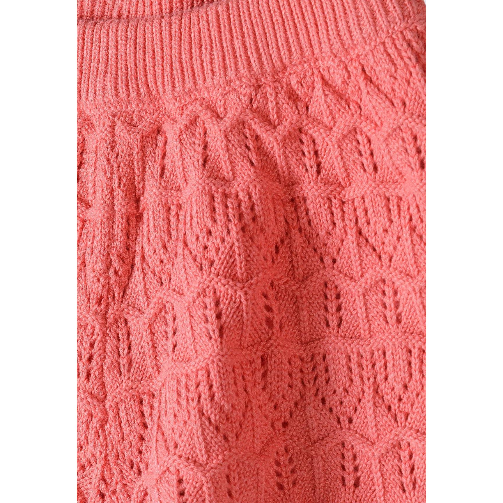Detailed texture shot of coral pink crochet fabric showing intricate leaf and diamond pattern stitching