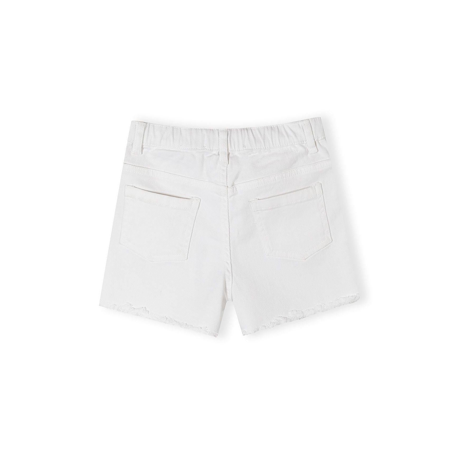 Close-up detail of white twill shorts showing Minoti brand label in waistband reading '6-7 YRS 110/116 CM MADE IN PAKISTAN' with button closure visible