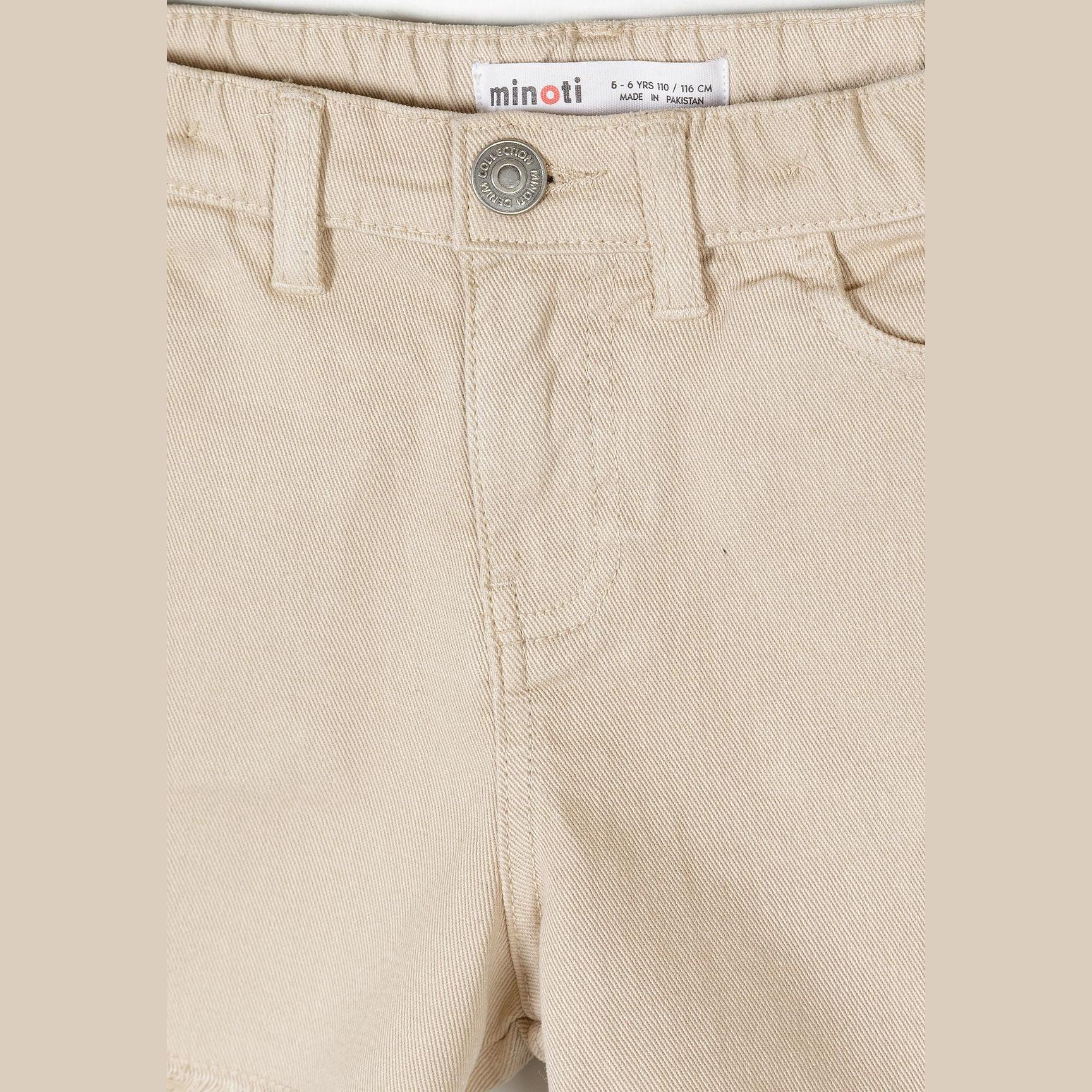 Close-up detail of beige shorts waistband showing Minoti label with size information, button fastening, and classic belt loops on neutral background