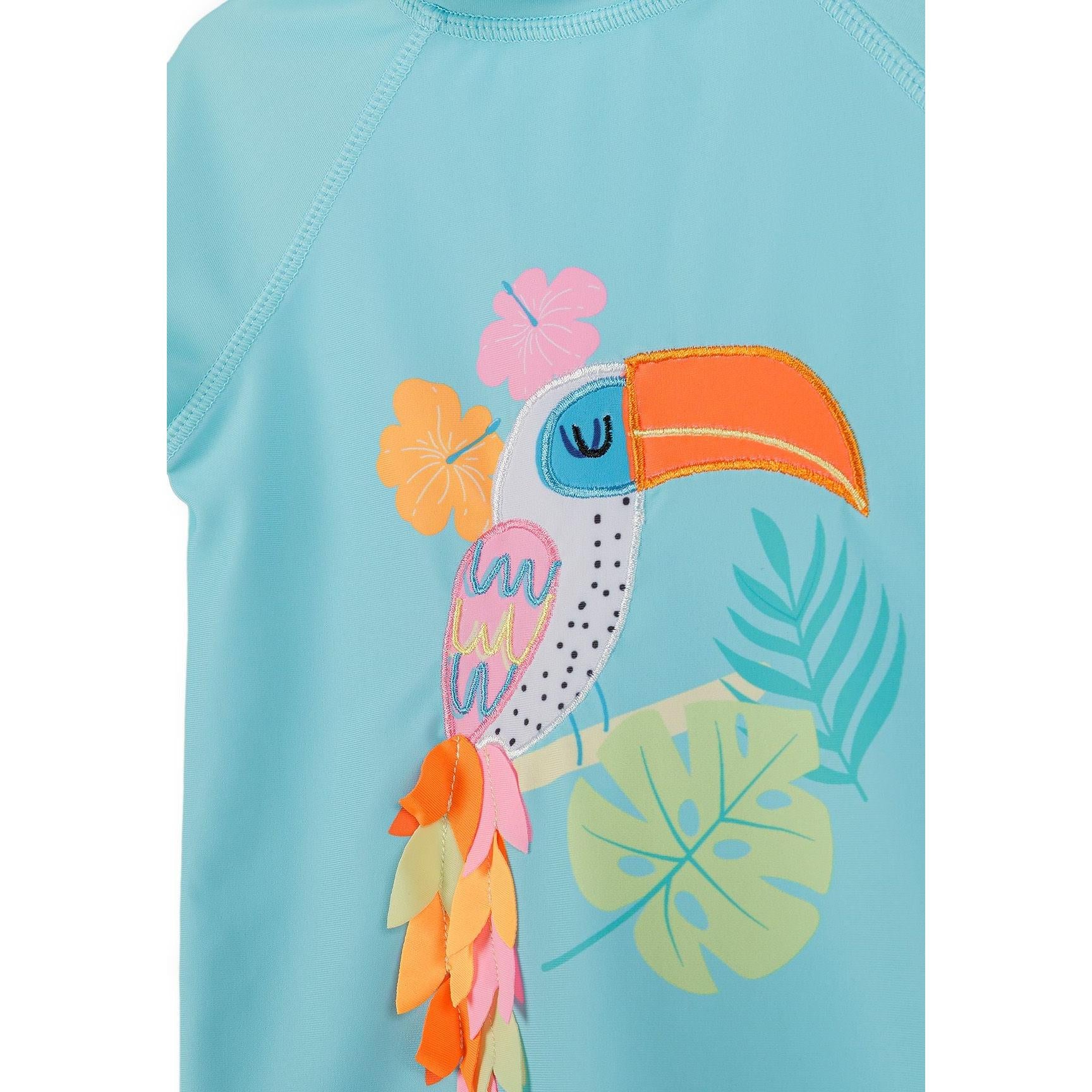 Close-up detail of tucan applique design showing tropical bird with orange beak surrounded by hibiscus flowers and palm leaves