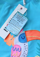 Close-up of turquoise fabric with colorful embroidered toucan design and sun protection label attached