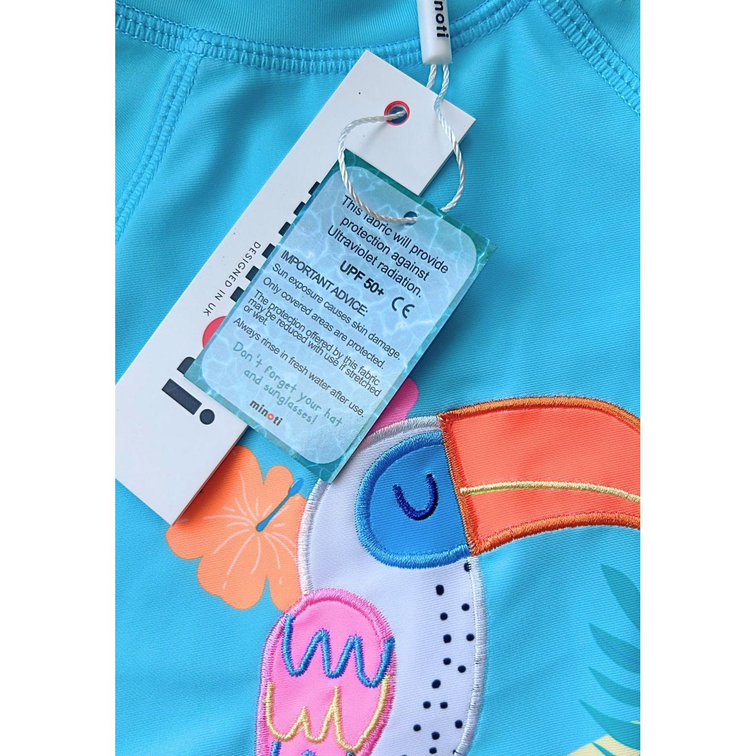 Close-up detail of tucan applique design showing tropical bird with orange beak surrounded by hibiscus flowers and palm leaves