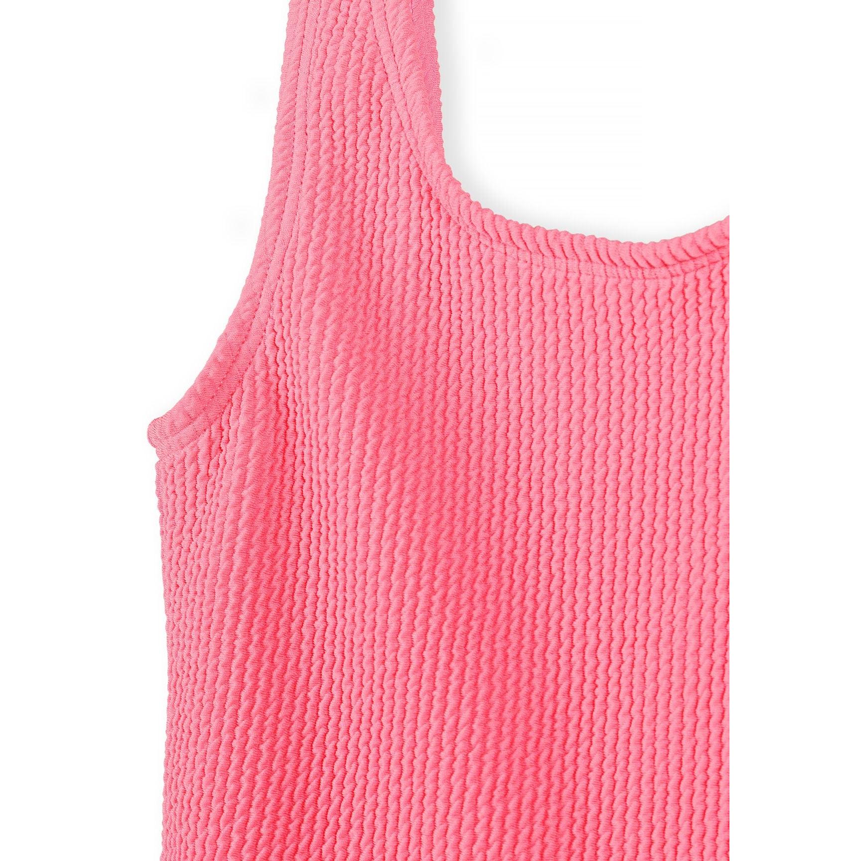 Close-up detail of coral pink ribbed swimsuit fabric showing textured surface and tie shoulder strap against white background