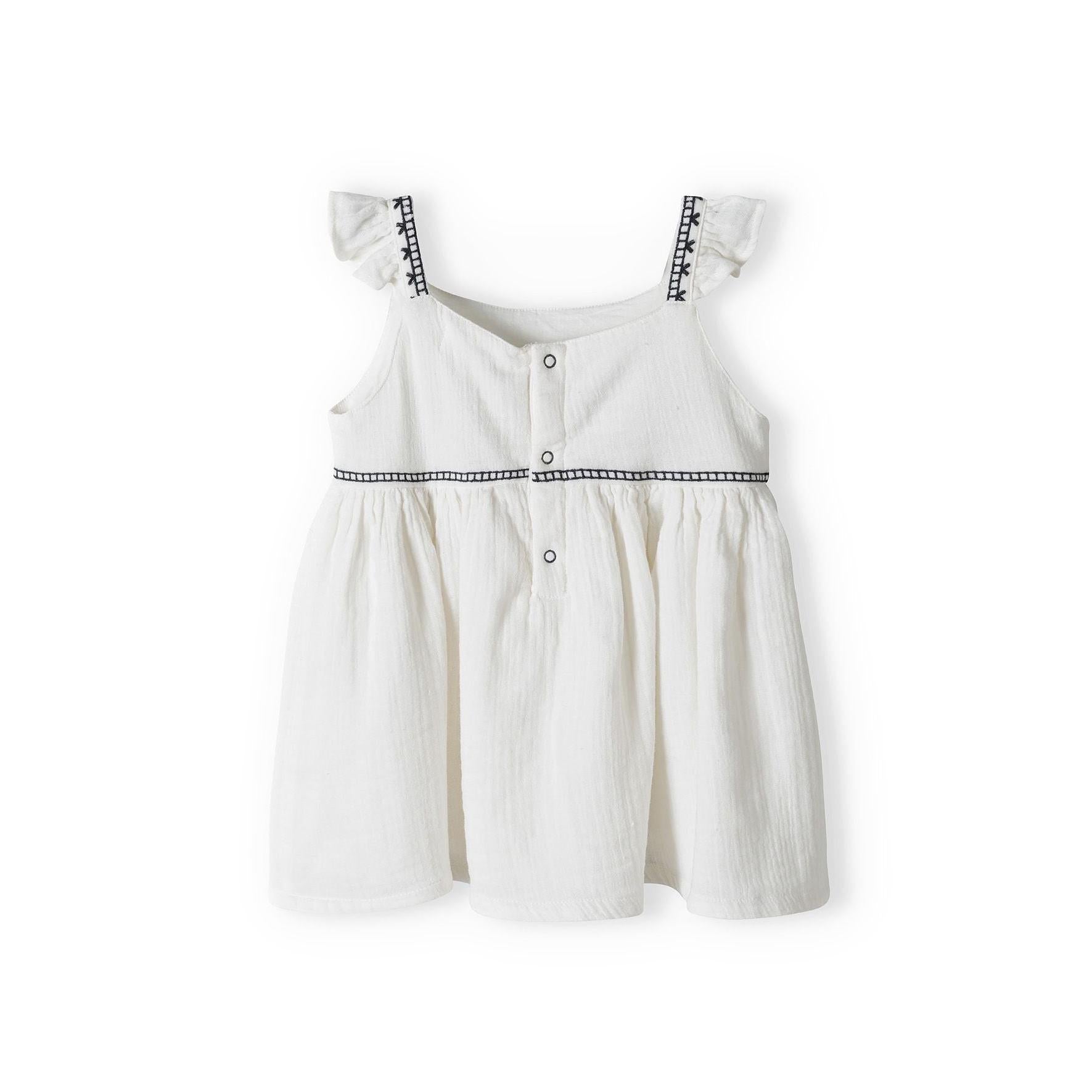 Flat lay of cream sleeveless top with decorative black embroidered trim and button front closure on white background