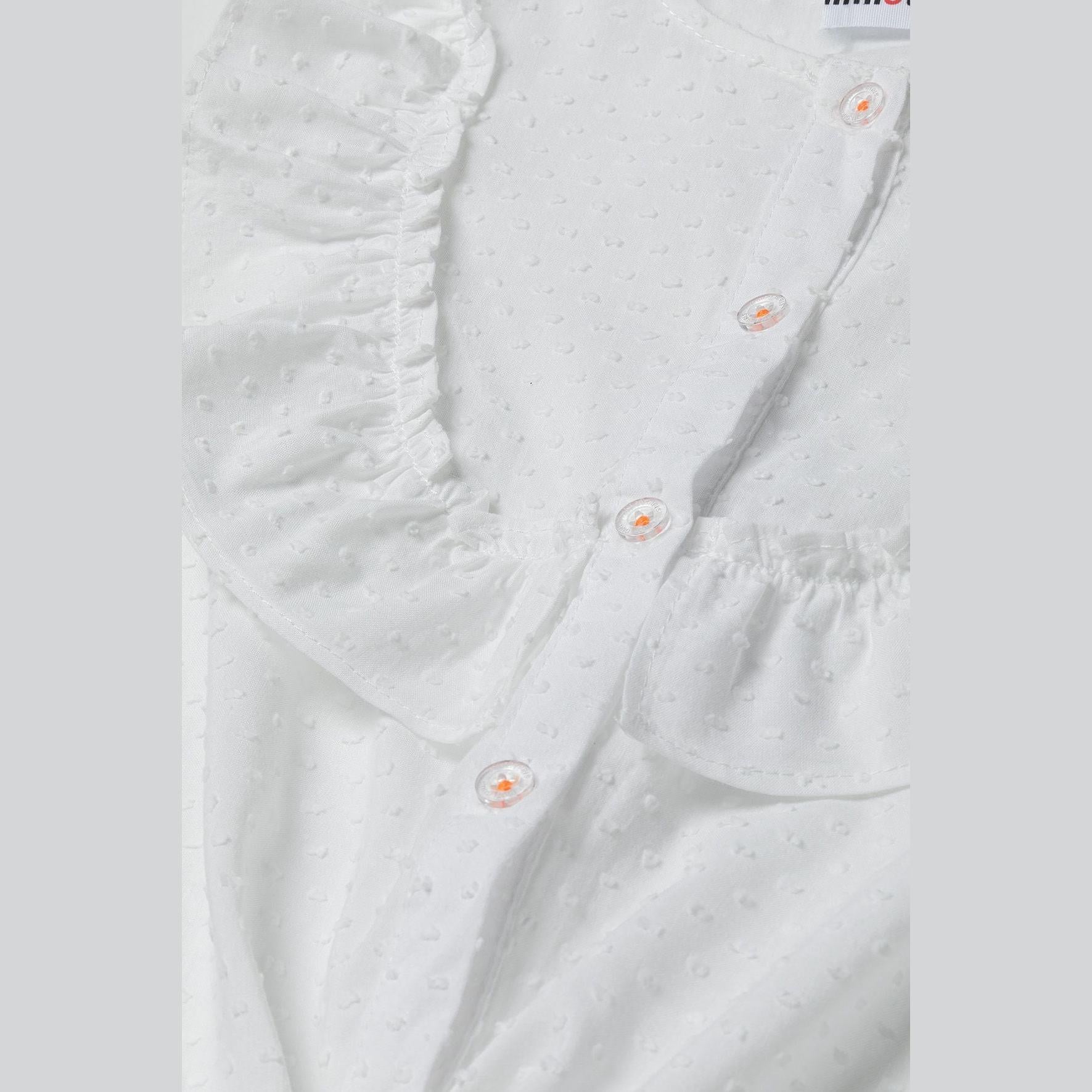 Close-up detail of white broderie anglaise fabric showing button fastening with small white buttons and delicate eyelet embroidery pattern
