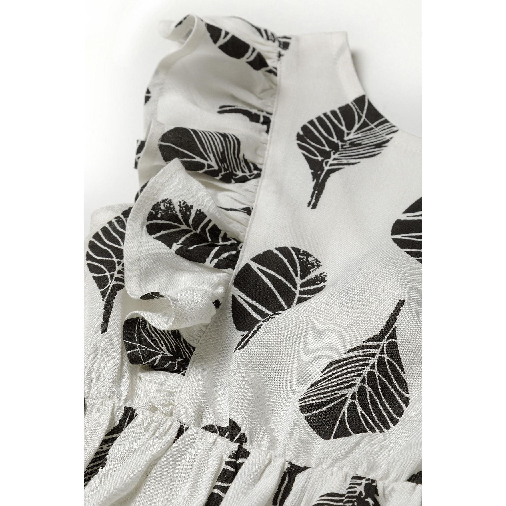 Close-up detail of white fabric showing black leaf print pattern and frill trim texture