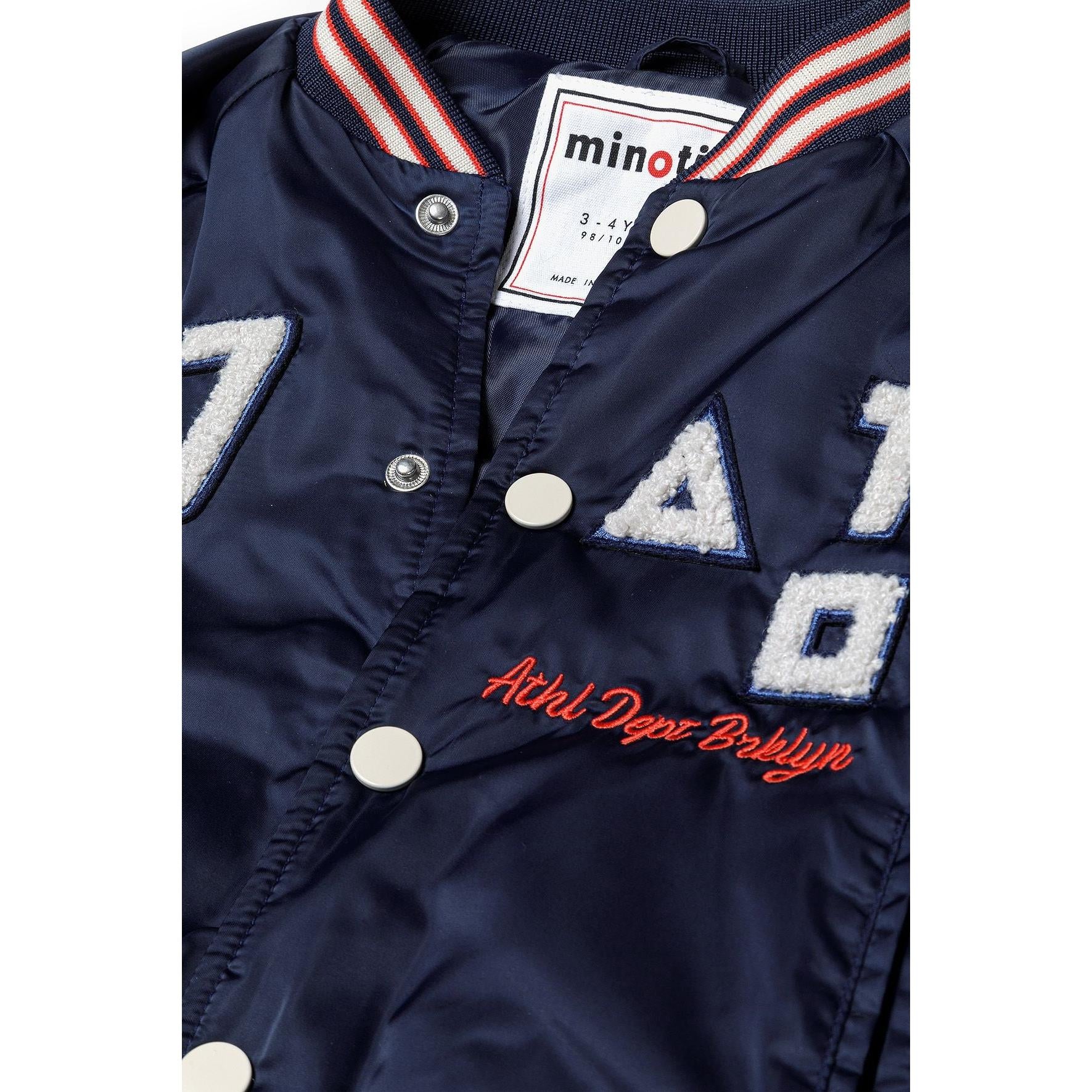 Close-up detail of navy bomber jacket showing Minoti label, snap buttons, and '97' appliqué with red embroidered text