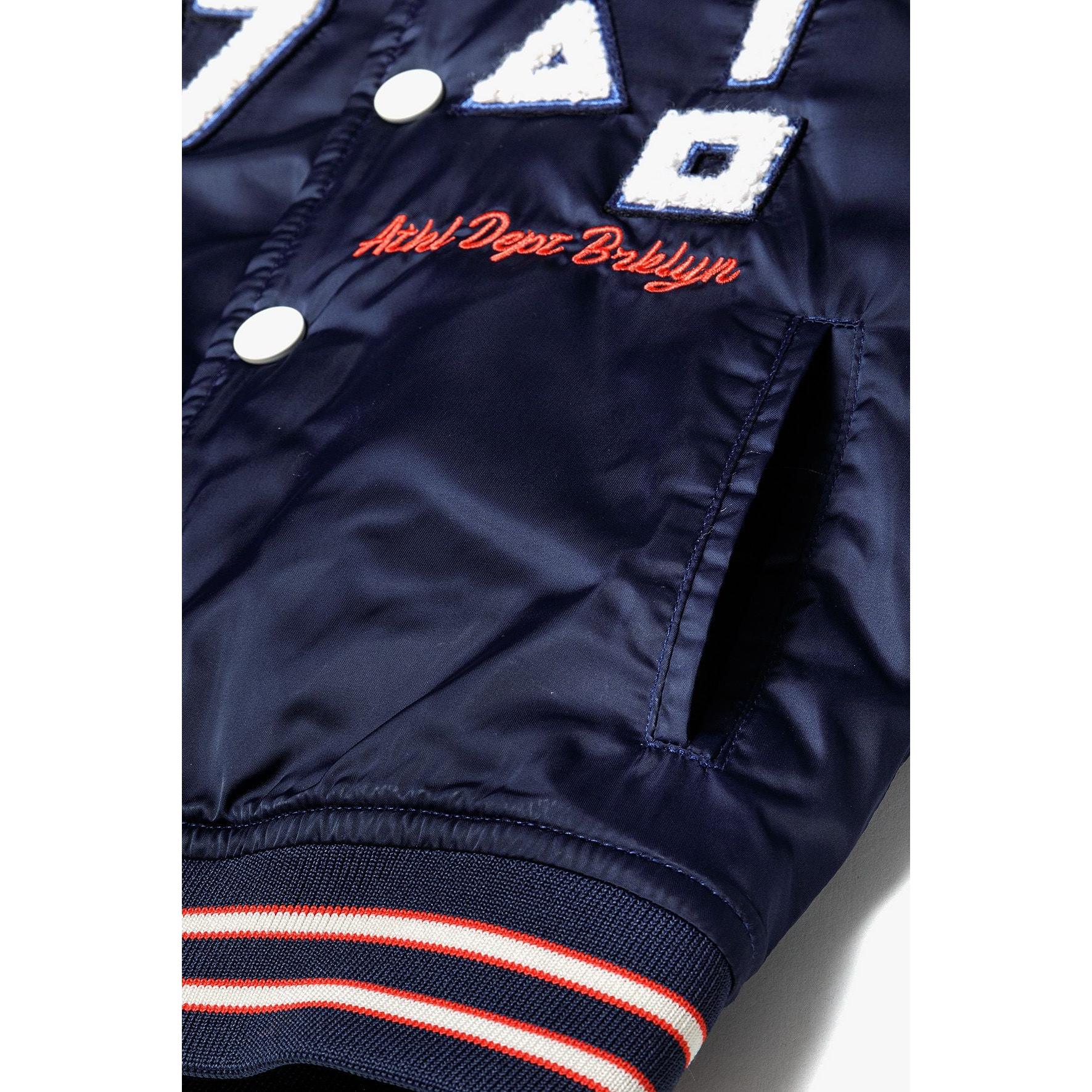 Close-up detail of navy bomber jacket showing Minoti label, snap buttons, and '97' appliqué with red embroidered text