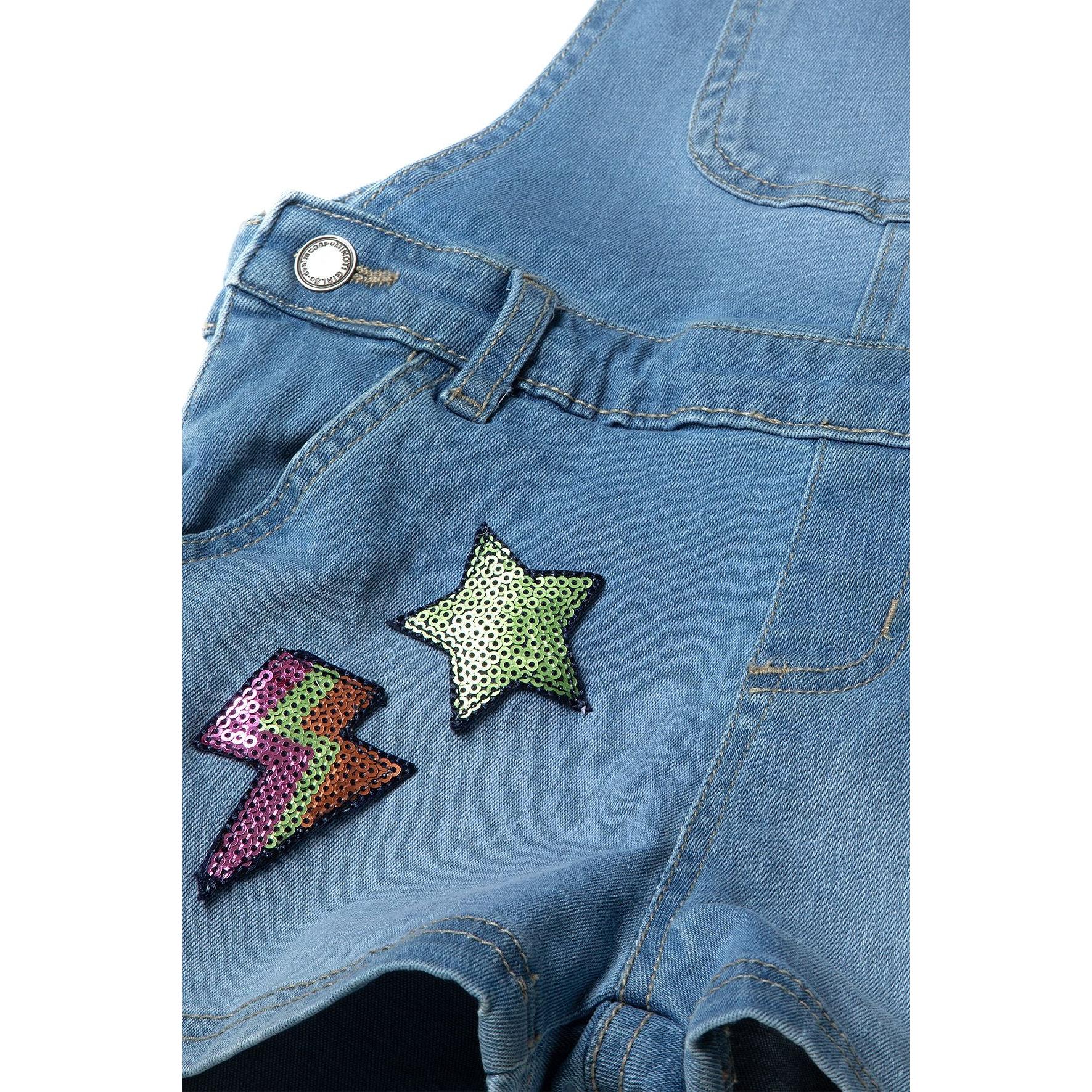 Close-up detail of denim dungarees front showing sequin star patch and lightning bolt appliqué with silver button fastening