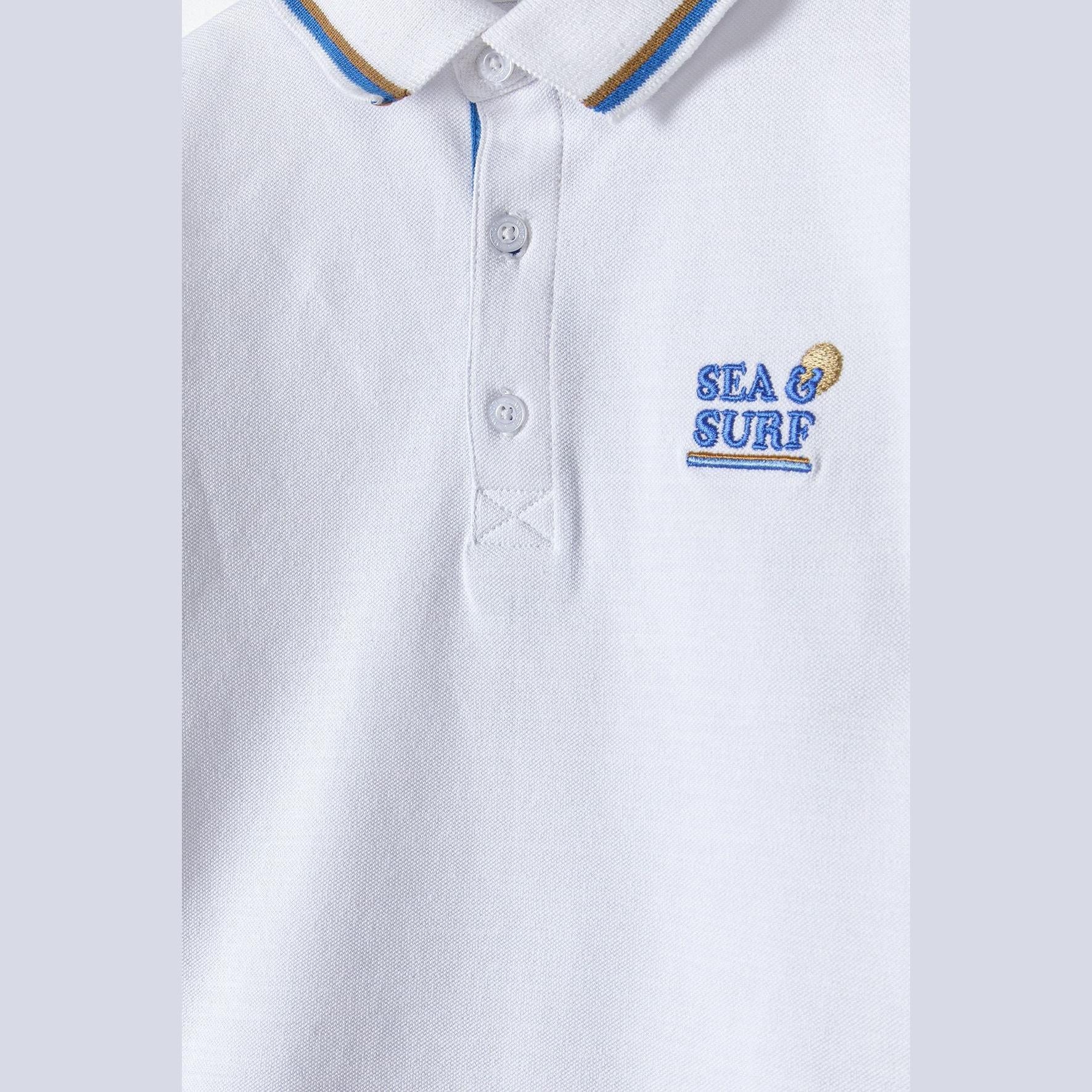 Close-up detail of white polo shirt showing Sea & Surf embroidered logo and three-button placket with blue inner details