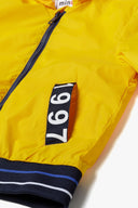 Bright yellow boys windbreaker jacket with hood, featuring contrast zip, elasticated hem, and stylish patch detail. Boys windbreaker jacket with hood yellow 1-14y.