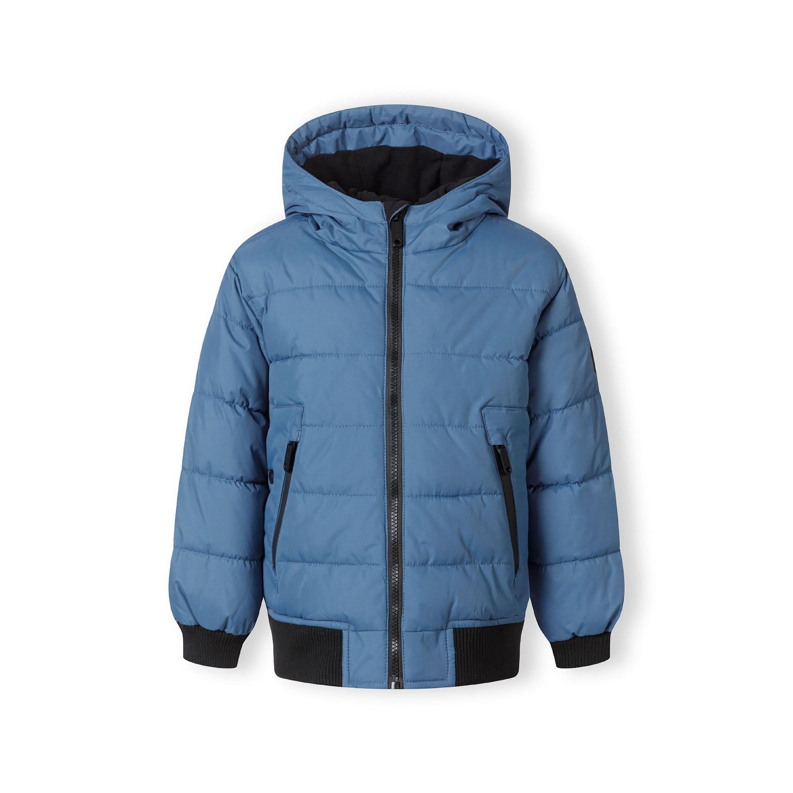 Close-up detail of blue padded jacket showing circular Minoti logo patch with cross design