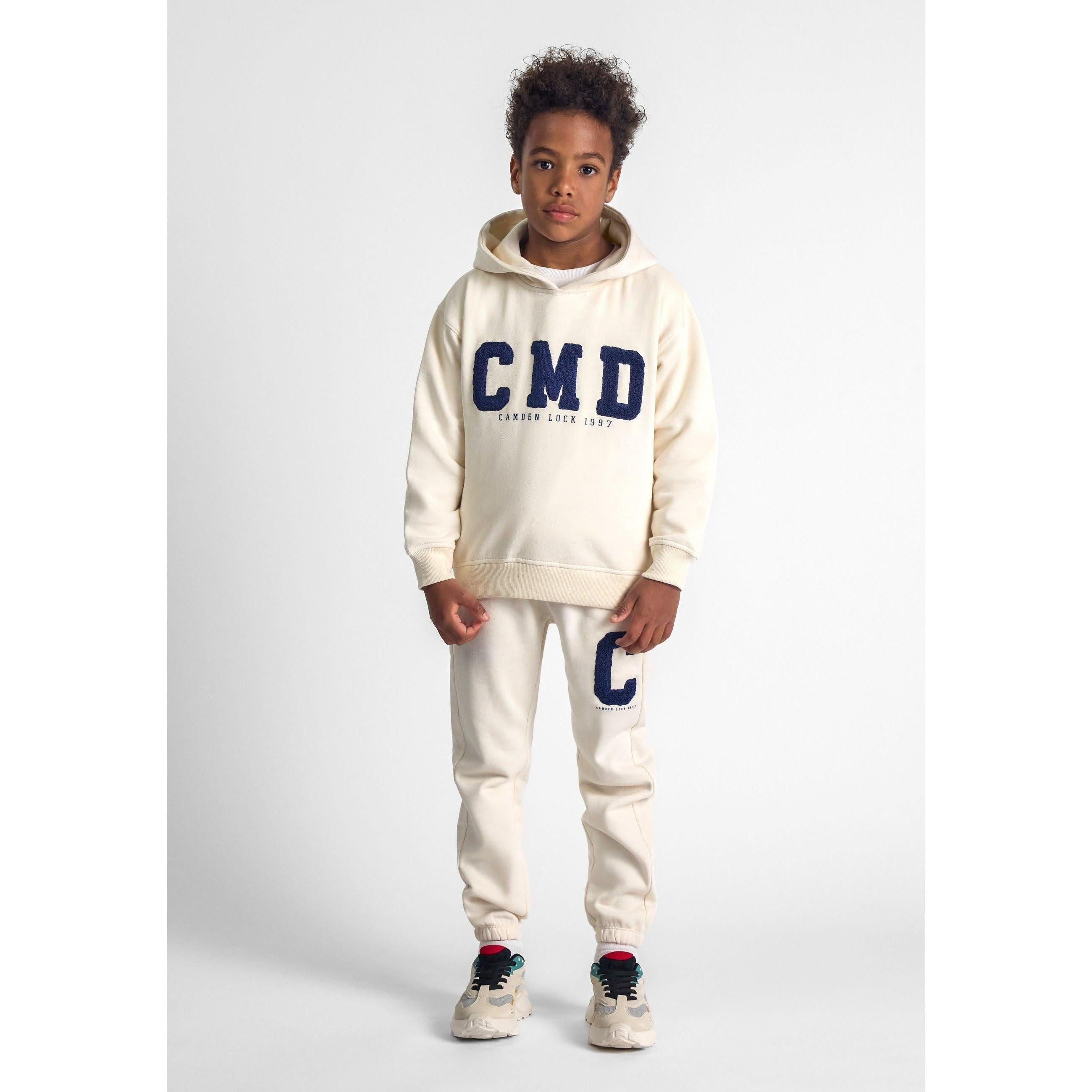 Young model wearing cream tracksuit set with CMD boucle embroidery on hoodie and C on joggers, standing against white background