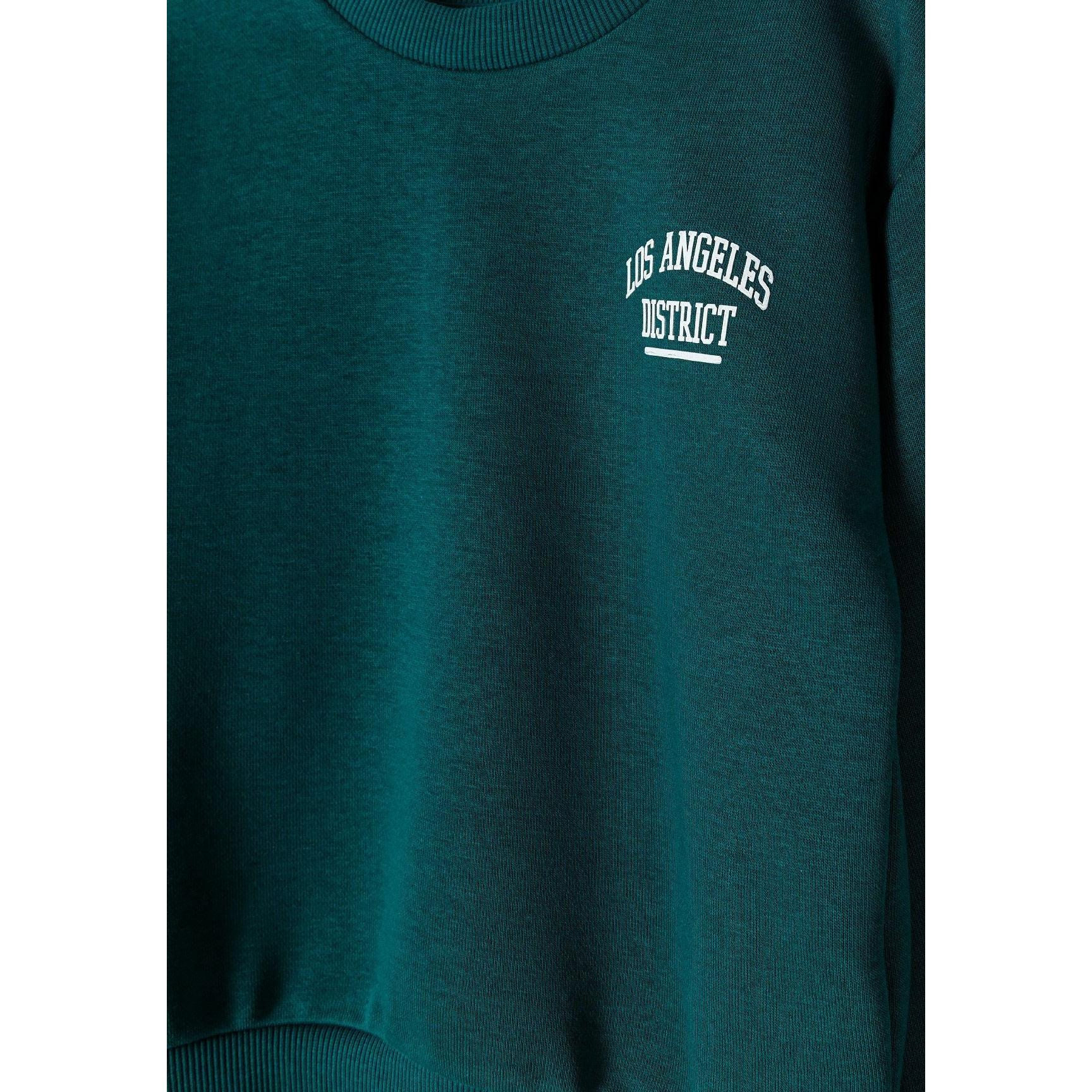 Close-up detail of dark green joggers showing elasticated waistband with drawstring and Los Angeles District white text print