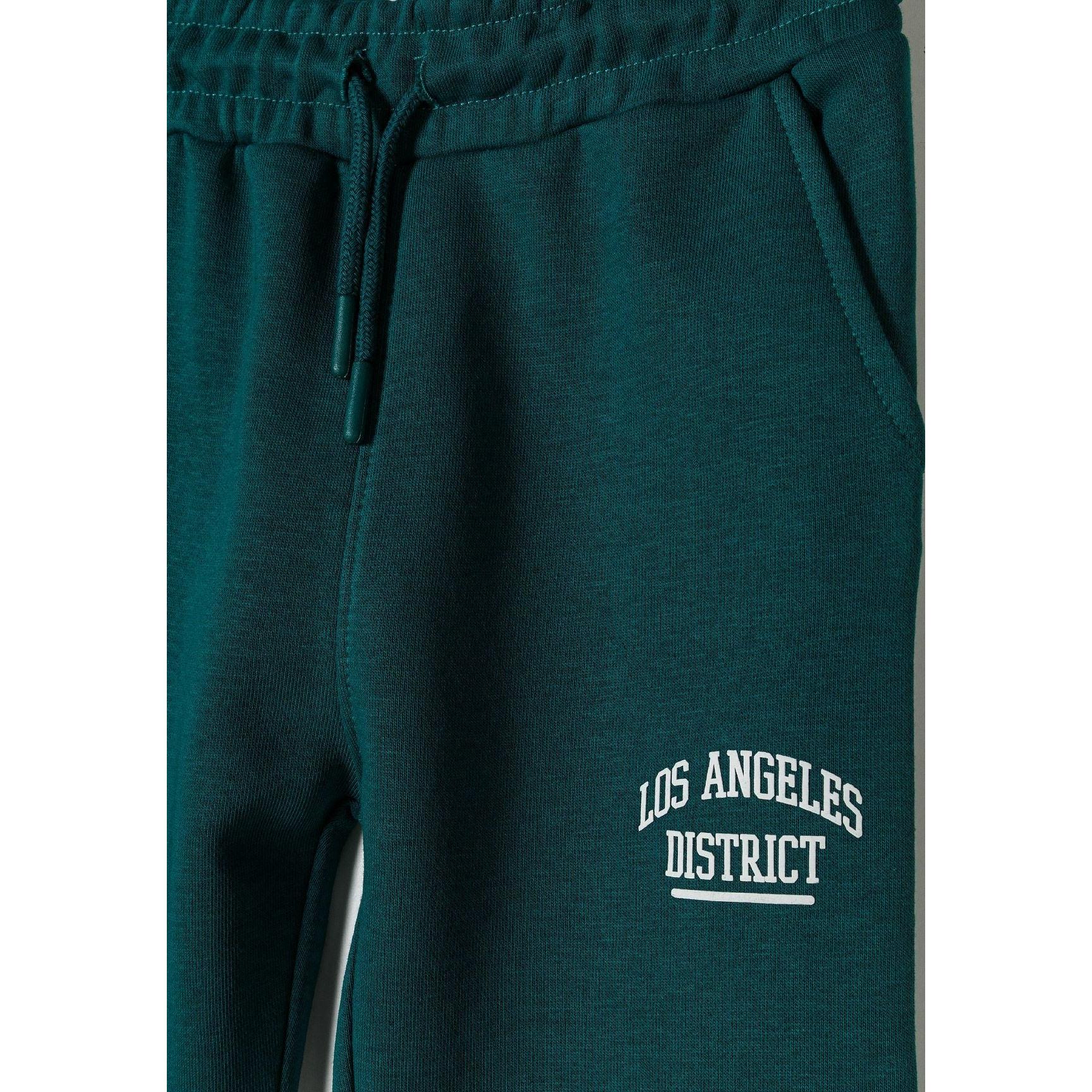 Close-up detail of dark green joggers showing elasticated waistband with drawstring and Los Angeles District white text print