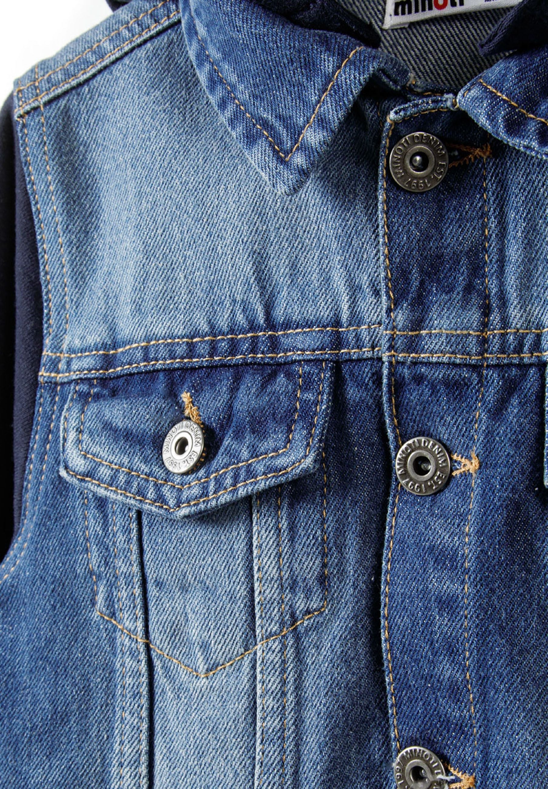 Close-up detail of navy denim jacket front showing button closure, chest pockets and Minoti label with contrast stitching