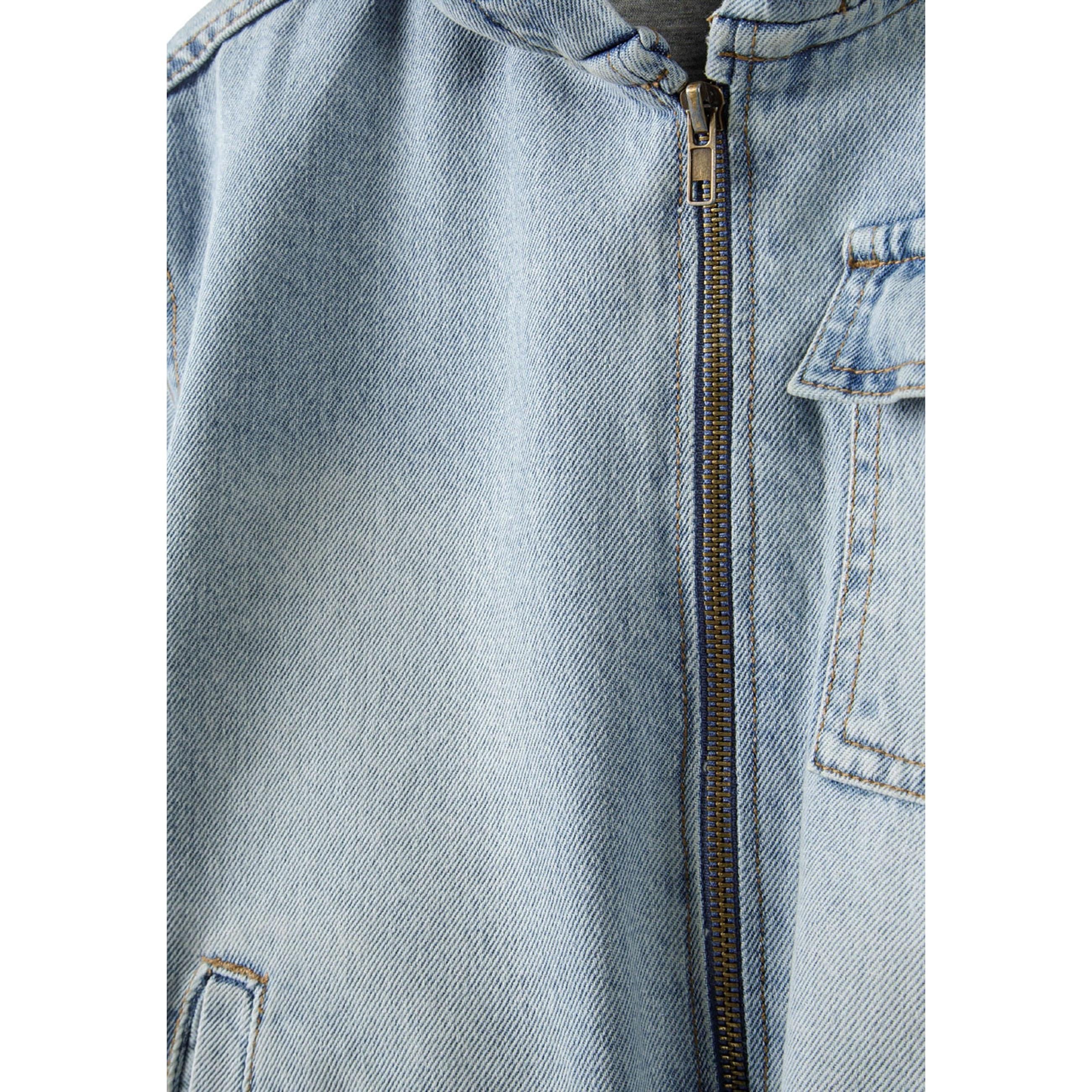 Close-up detail of light blue denim jacket showing zip closure and chest pocket with classic denim stitching