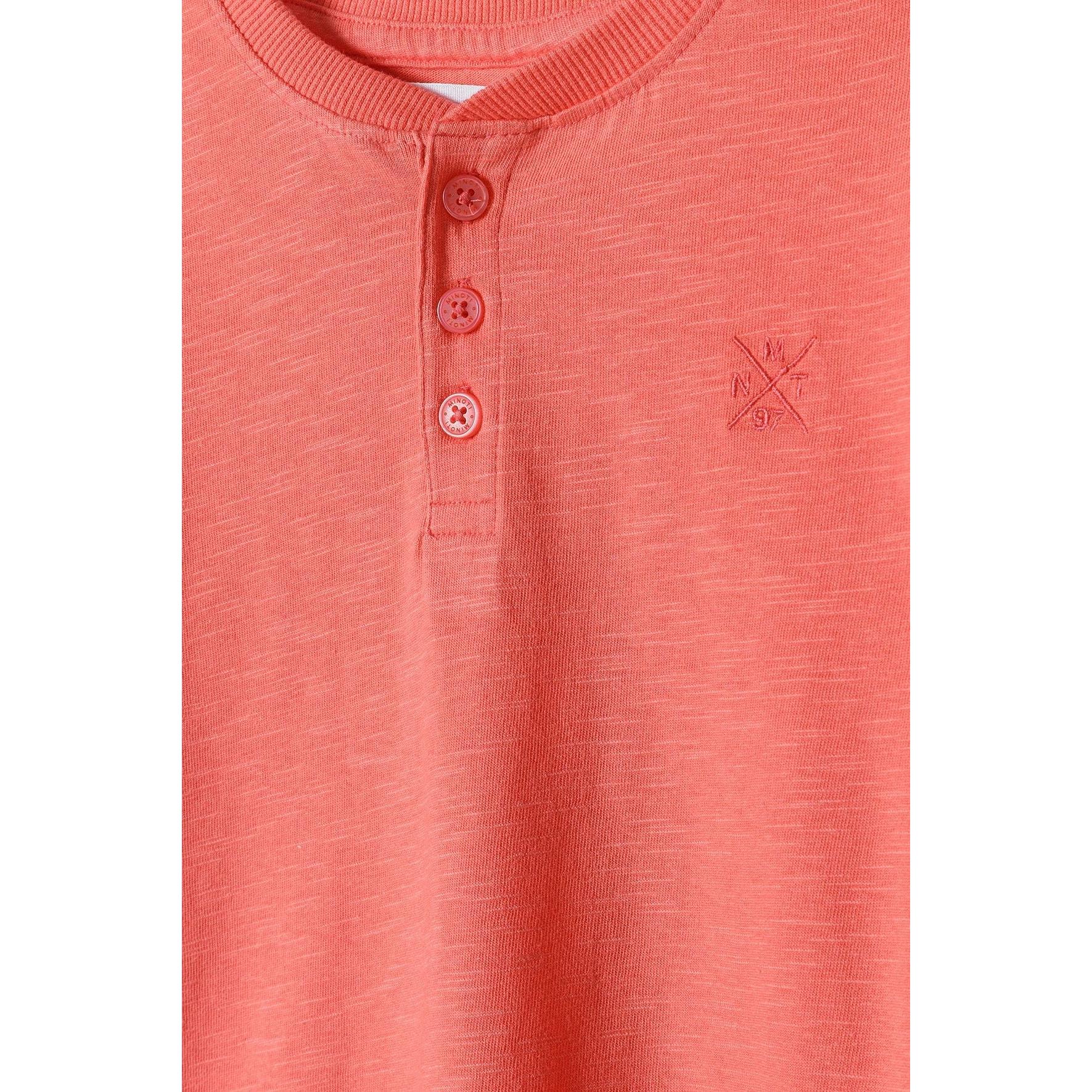 Close-up detail of coral henley t-shirt showing button neck fastening and subtle logo embroidery
