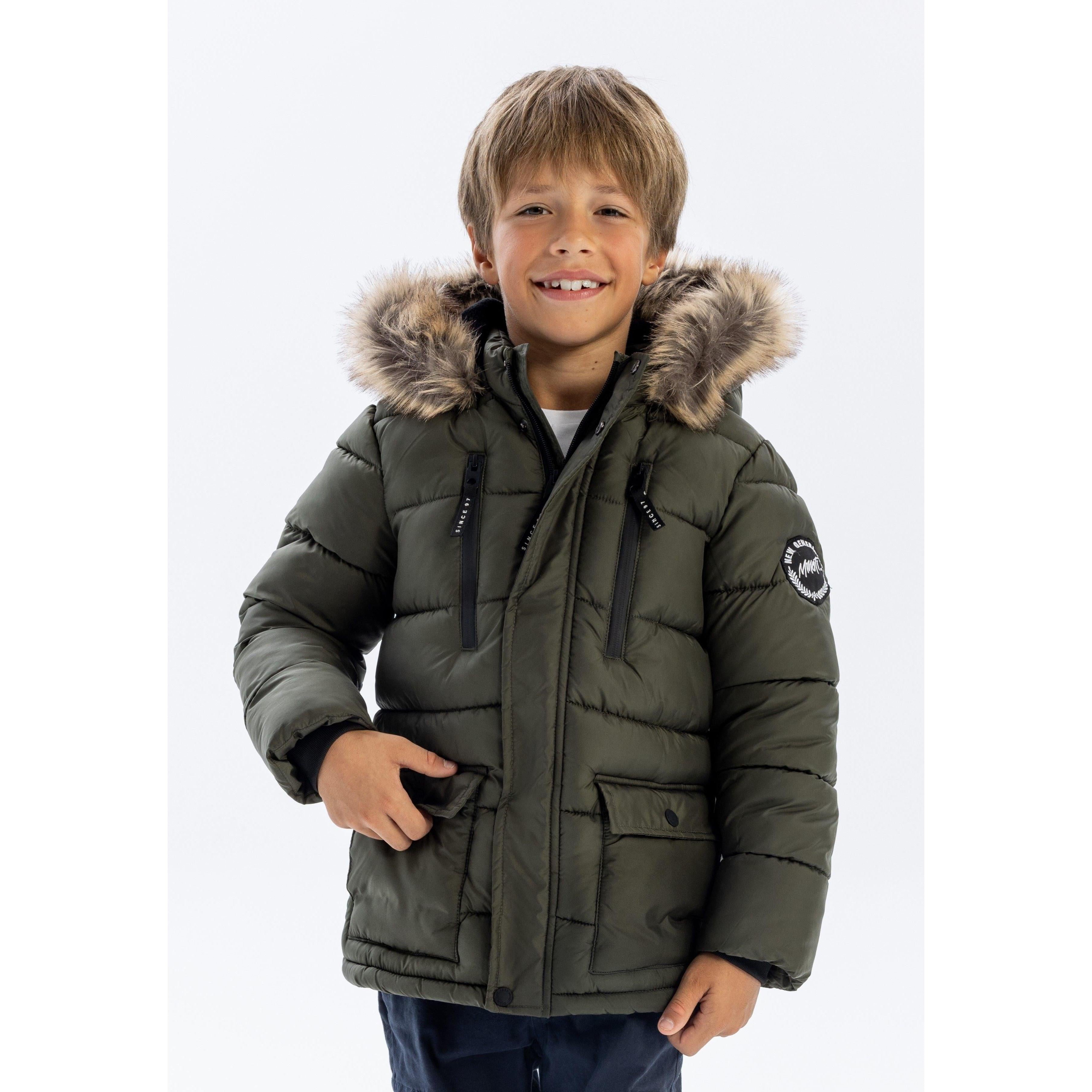 Young boy wearing khaki quilted parka jacket with faux fur hood, smiling at camera against white studio background