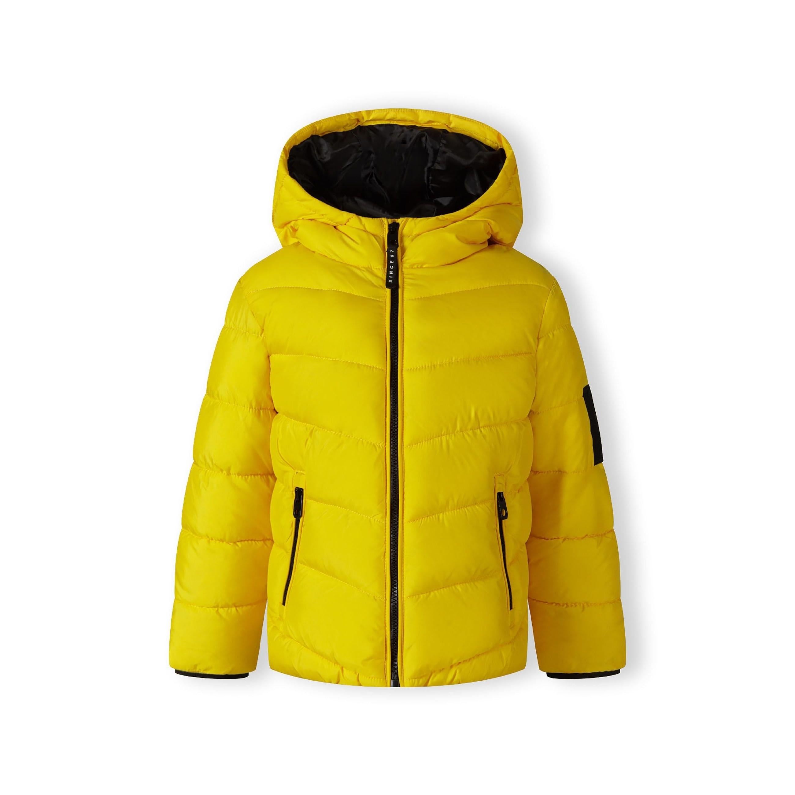 Close-up detail of black fabric label on yellow padded jacket showing Minoti brand text and sizing information