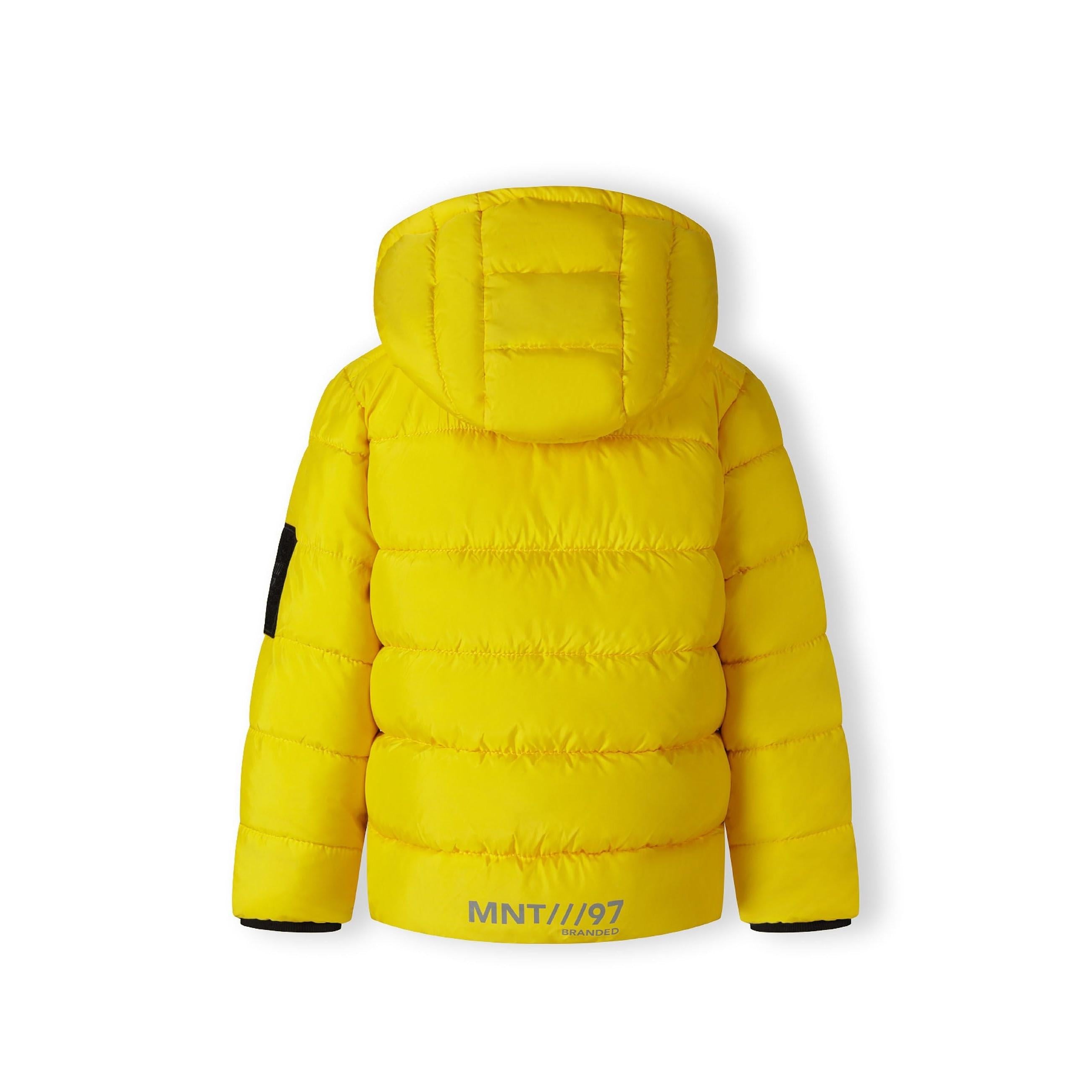 Close-up detail of black fabric label on yellow padded jacket showing Minoti brand text and sizing information