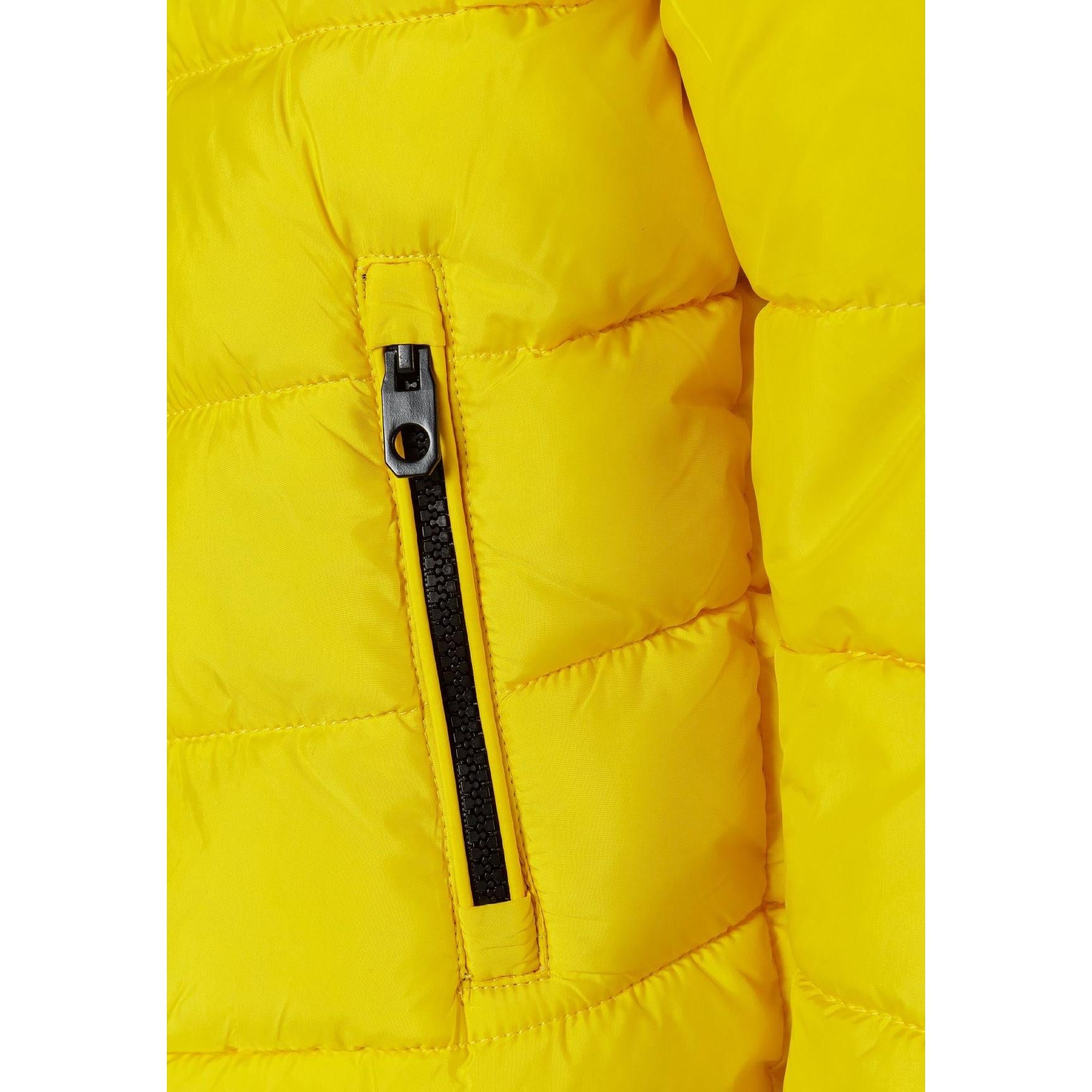 Close-up detail of black fabric label on yellow padded jacket showing Minoti brand text and sizing information