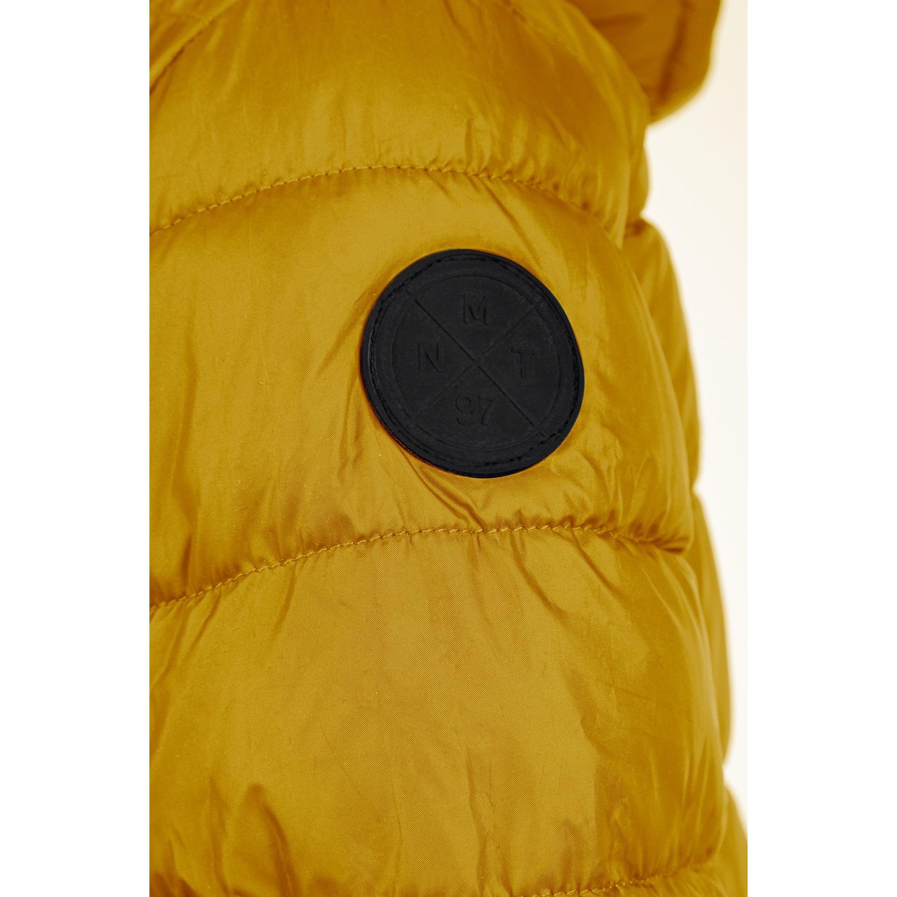 Detail shot of yellow padded jacket sleeve showing black circular logo patch on quilted fabric with horizontal stitching lines