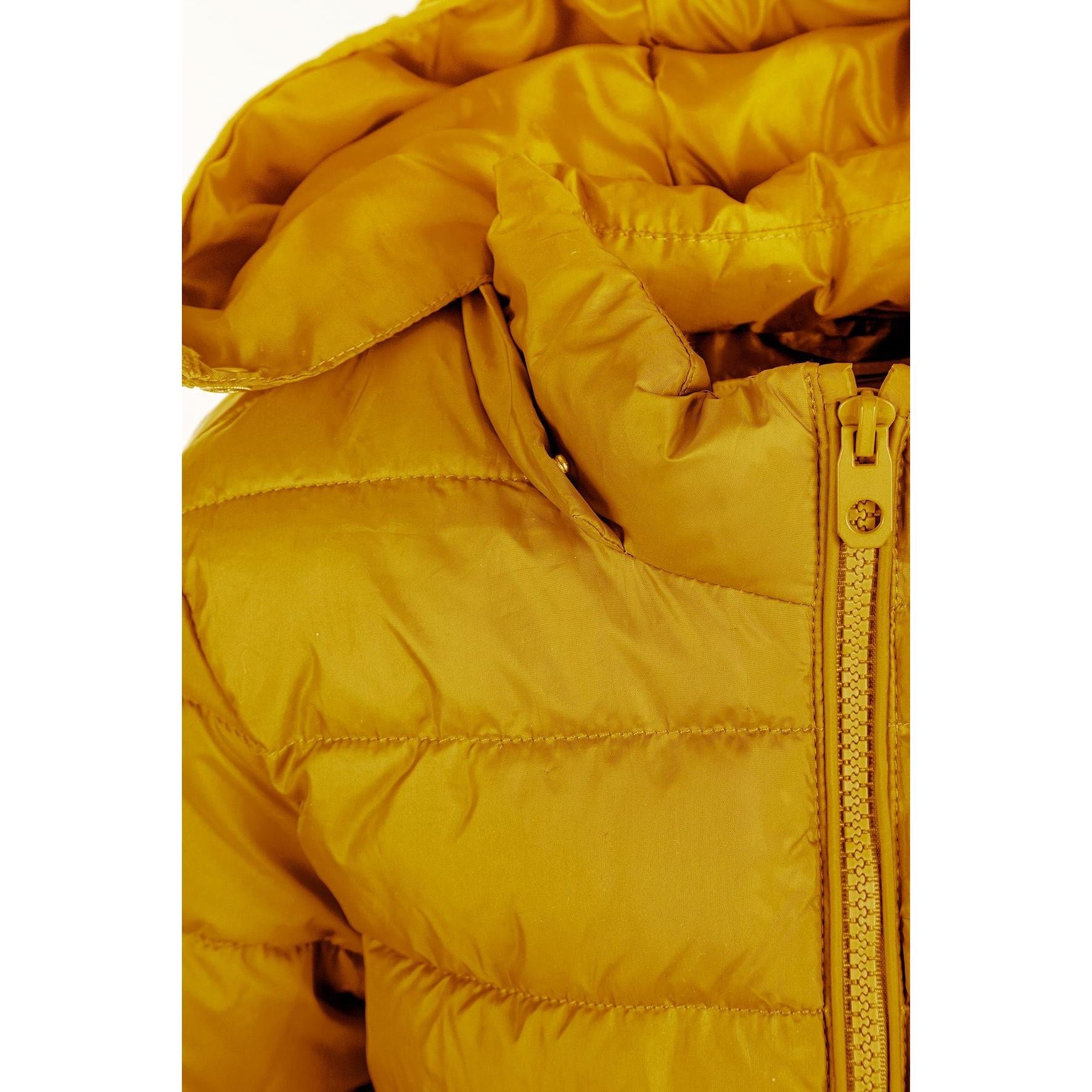 Detail shot of yellow padded jacket sleeve showing black circular logo patch on quilted fabric with horizontal stitching lines