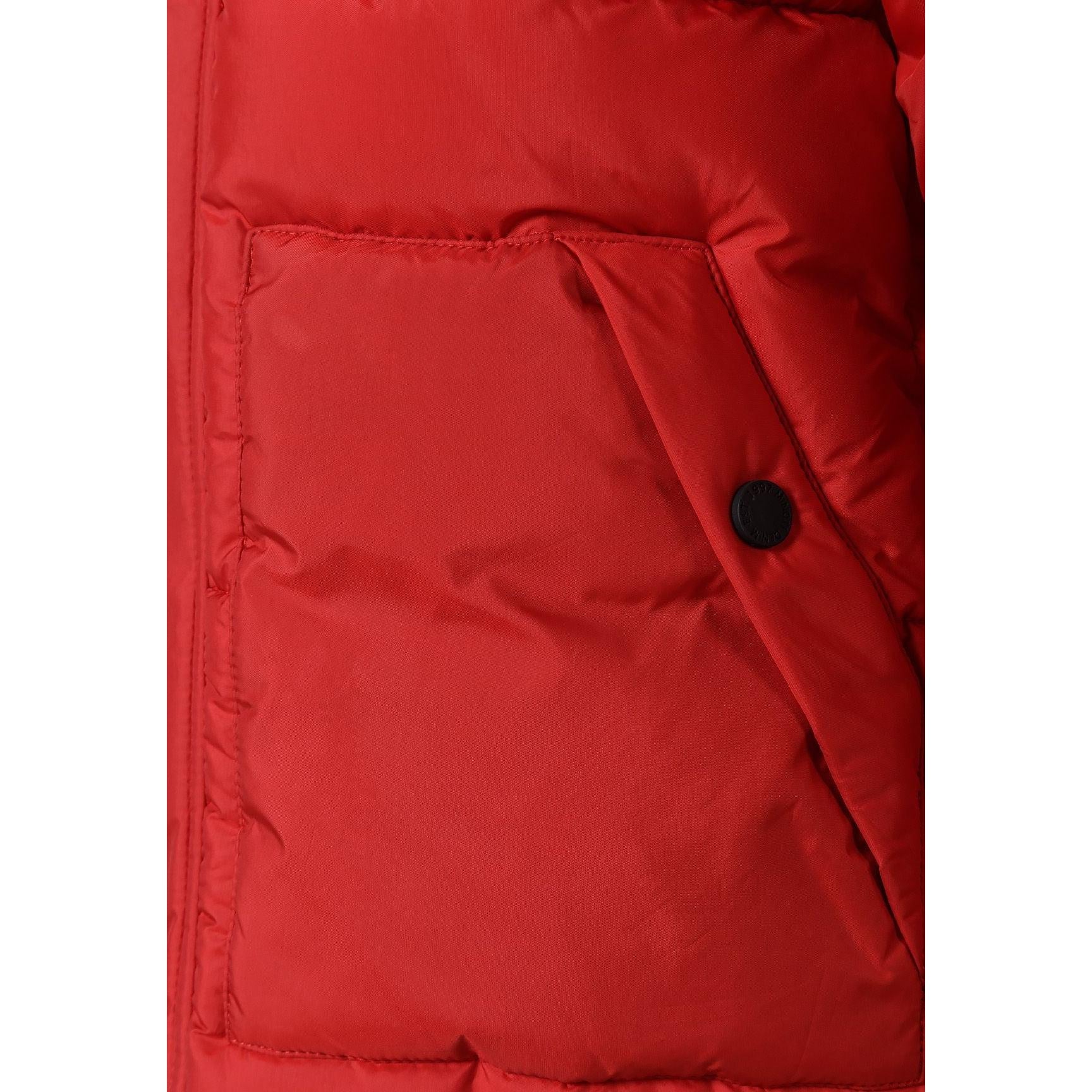 Close-up detail of black circular Minoti badge with crossed design and brand lettering on red padded jacket sleeve