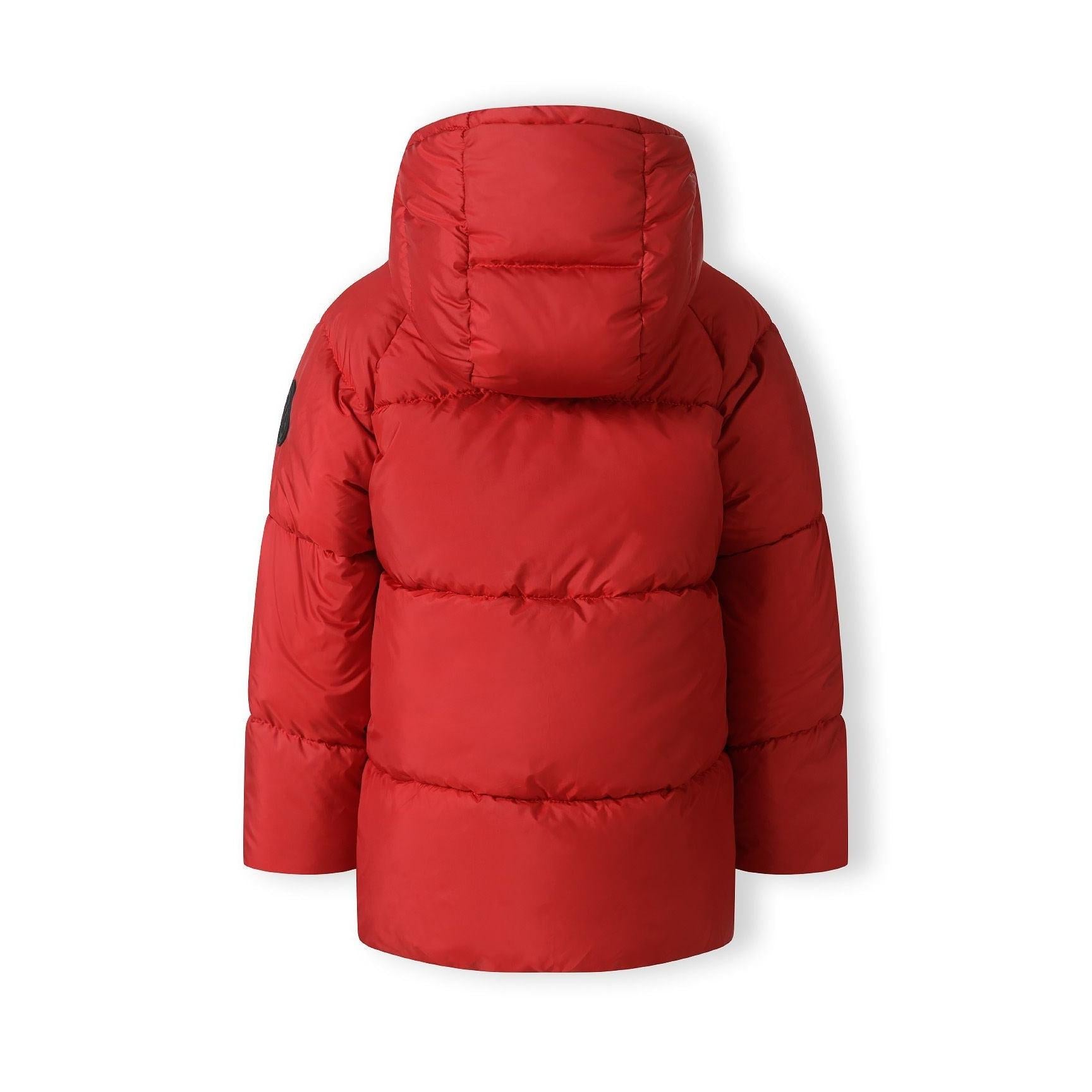 Close-up detail of black circular Minoti badge with crossed design and brand lettering on red padded jacket sleeve