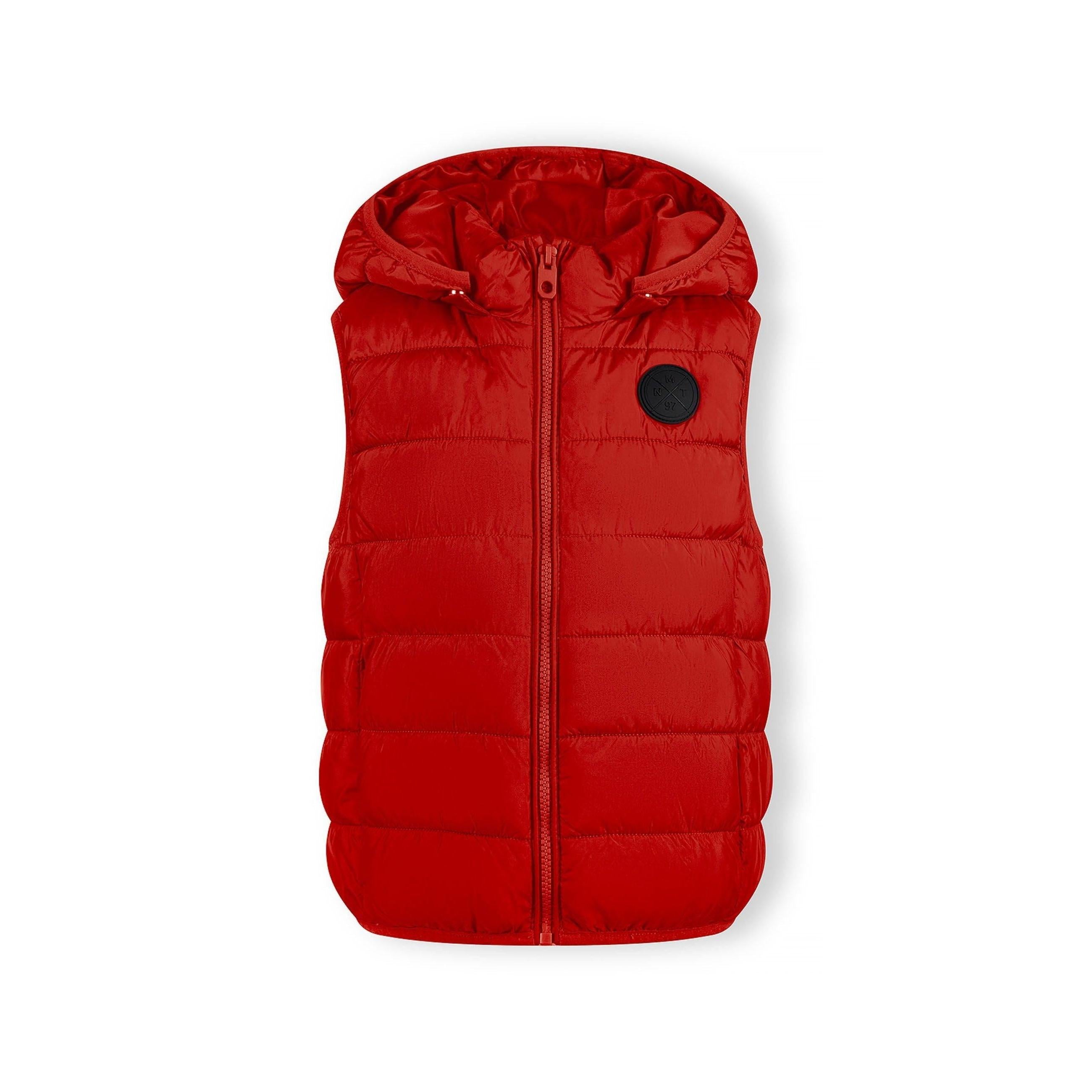 Boy in casual pose wearing red quilted gilet with hood over navy top and blue jeans against studio background