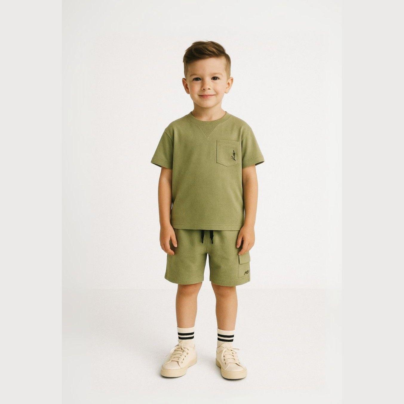 Young boy wearing olive green t-shirt and matching shorts set against white background, styled with striped socks and beige sneakers