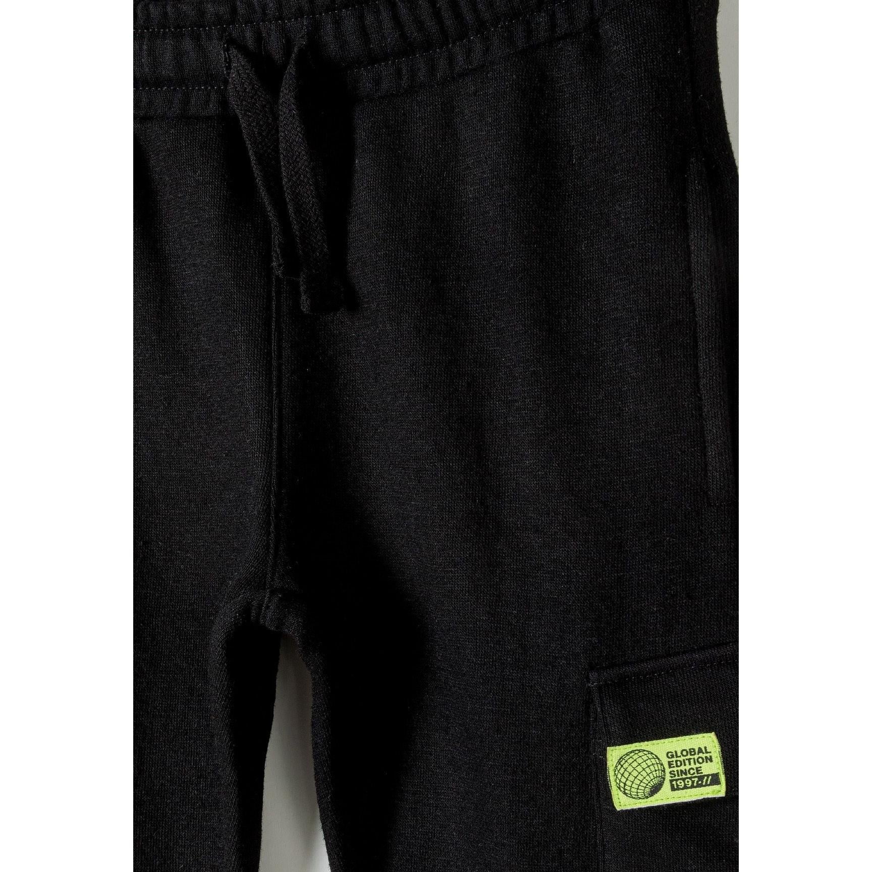 Close up detail of black fleece joggers showing drawstring waistband and green label patch