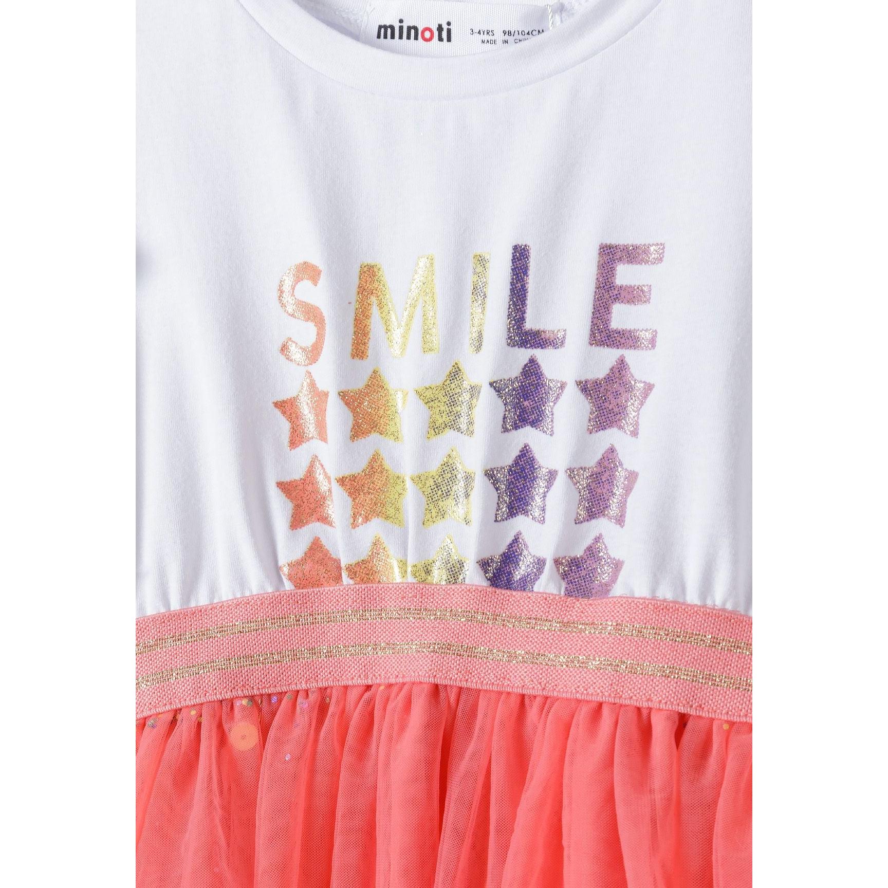 Close-up detail of white jersey bodice with rainbow glittery SMILE text and star pattern, showing coral mesh skirt edge