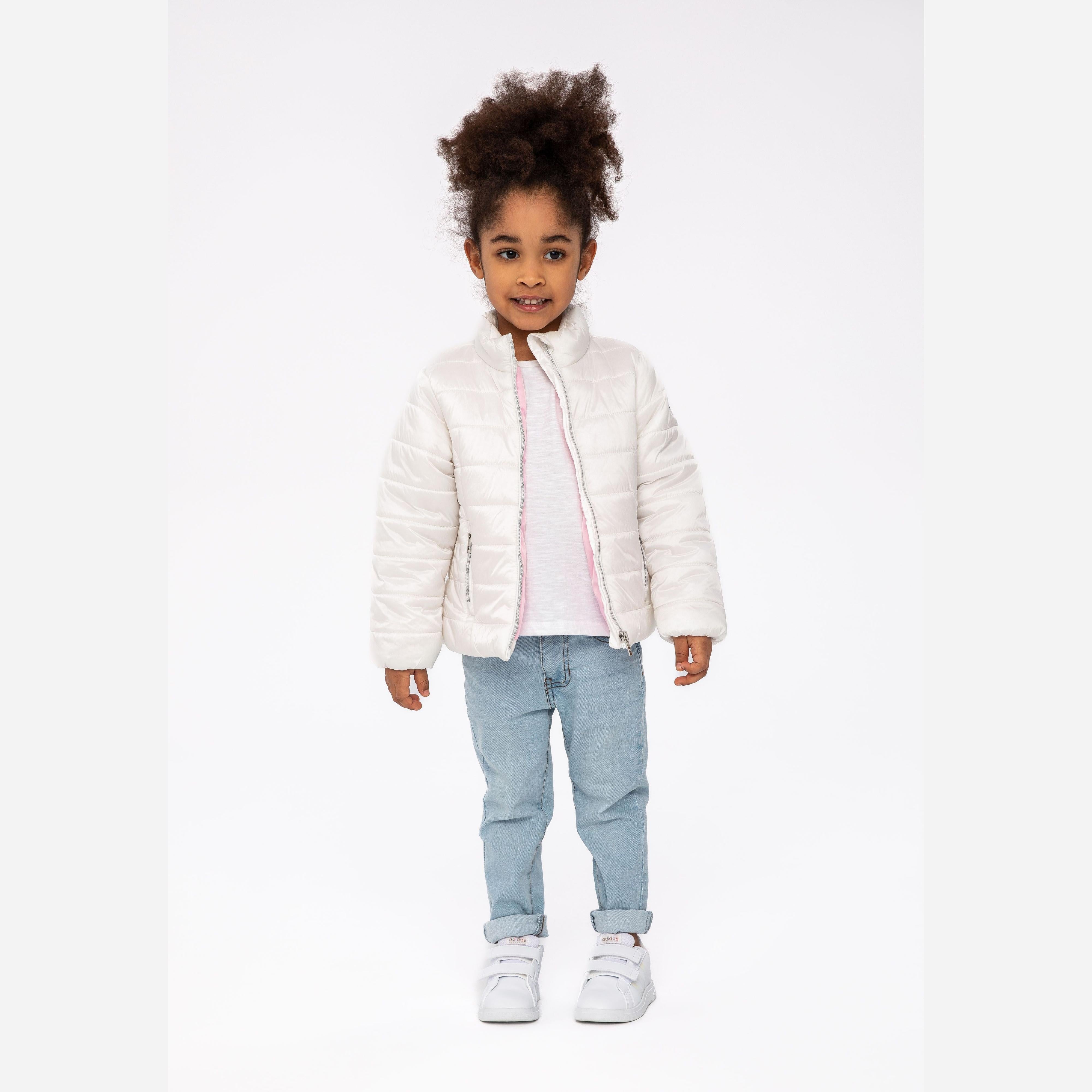 Young girl wearing cream quilted padded jacket with jeans and white trainers against white studio background