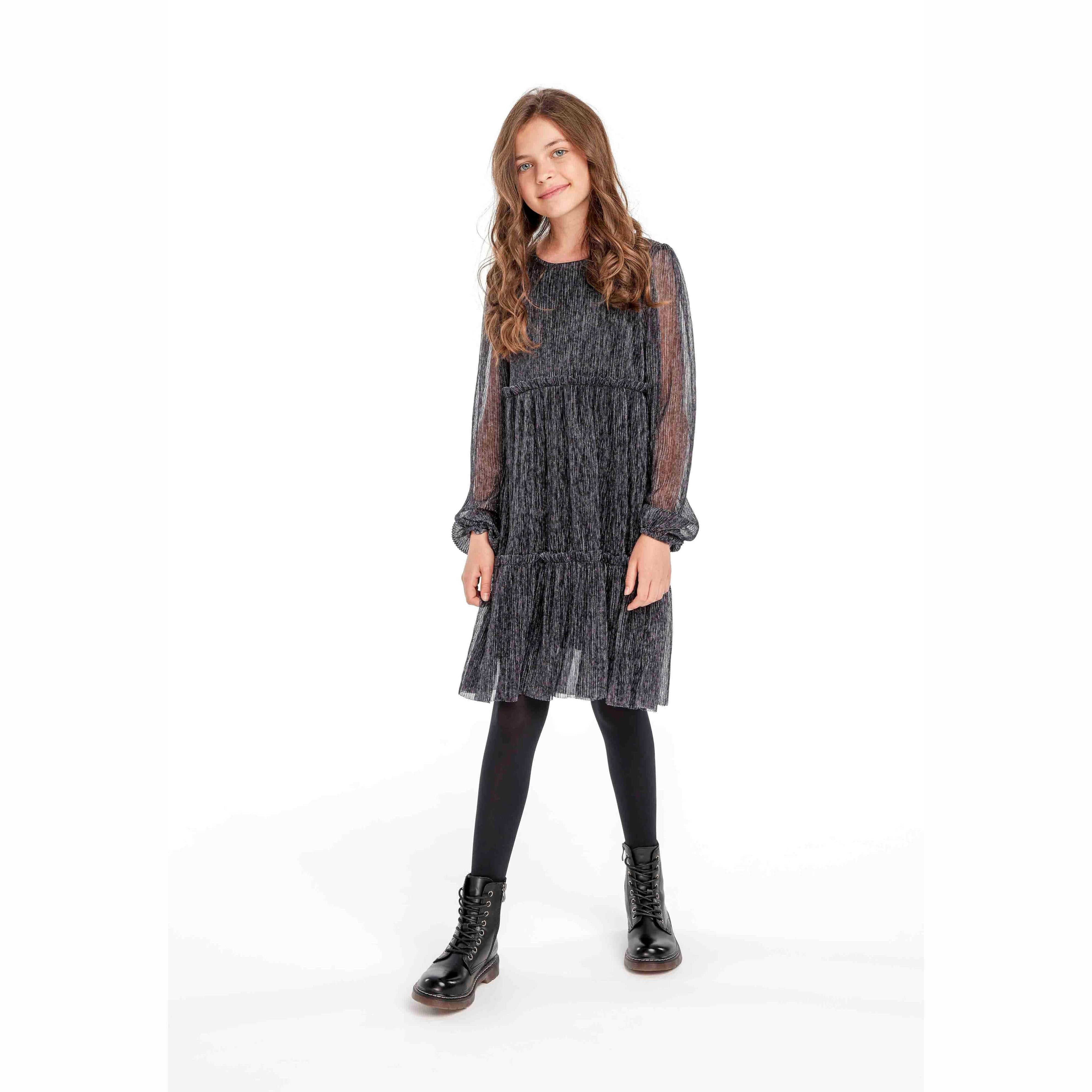 Young girl wearing black sparkle party dress with long balloon sleeves, styled with black tights and boots, full body shot on white background