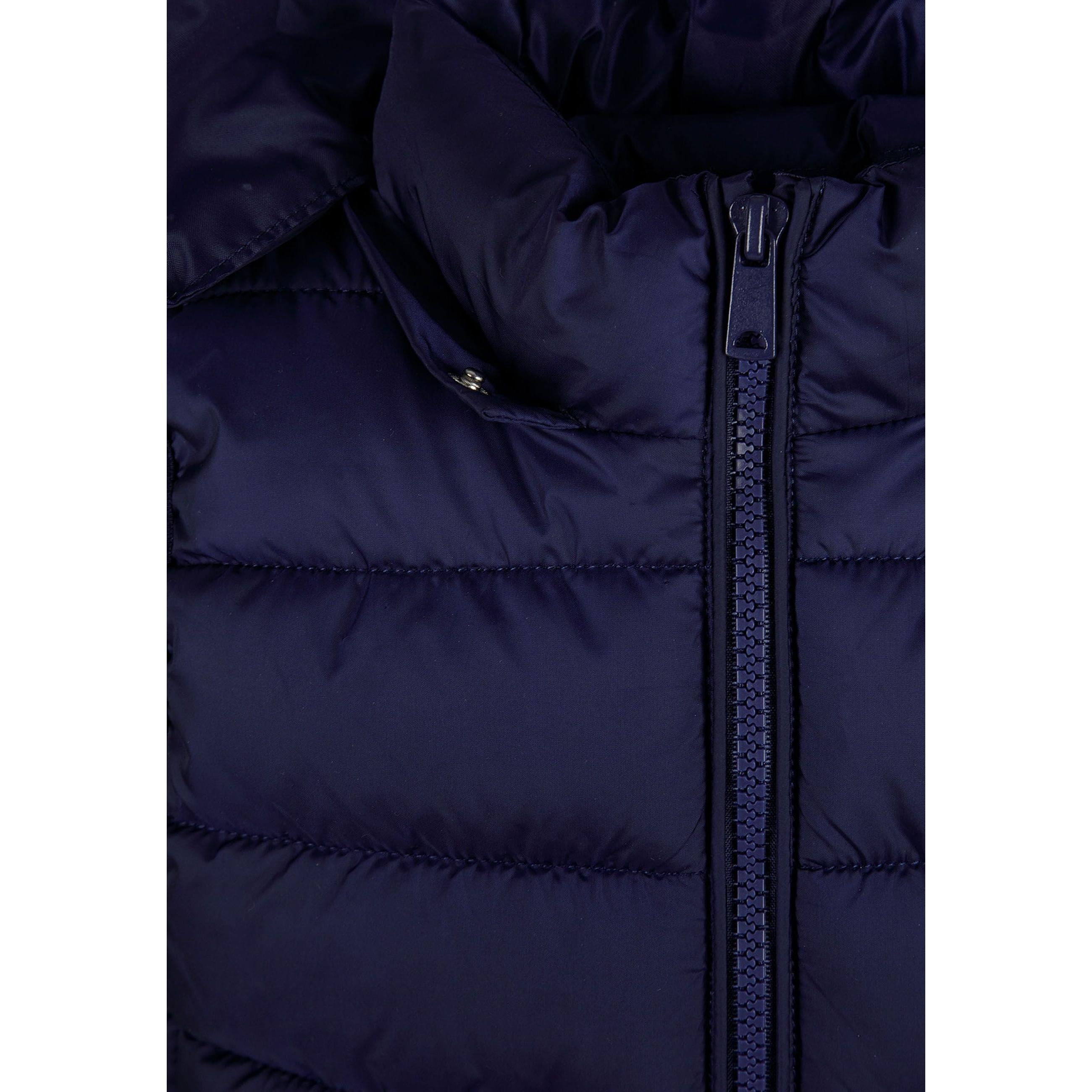 Close-up detail of navy quilted fabric texture showing stitched panels and holographic Minoti brand patch